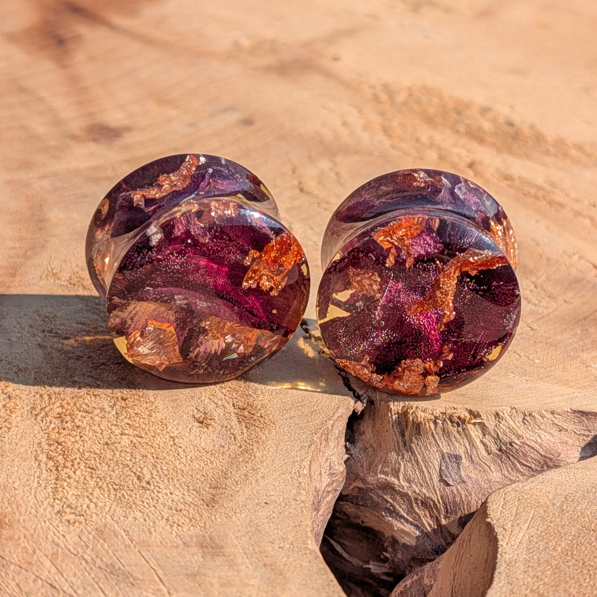 Pair of purple and orange gemstone earrings on a beige stone surface