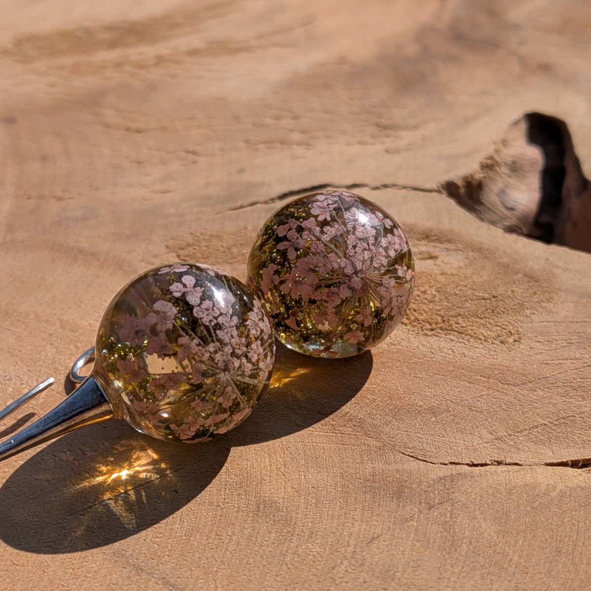 Close-up of dried white flowers and moss inside clear resin ball earrings, EL Creations Belgium