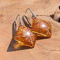 Pair of amber-colored square earrings on a wooden surface