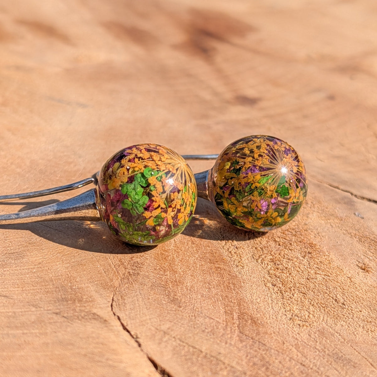 Close-up of mixed dried flowers and moss inside clear resin ball earrings, botanical jewelry EL Creations