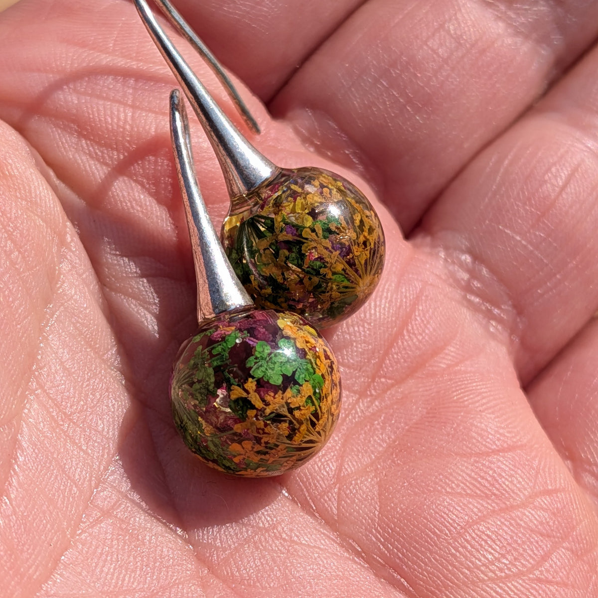 Handmade mixed flower moss resin ball earrings held between fingers, 3cm dangle jewelry EL Creations Belgium
