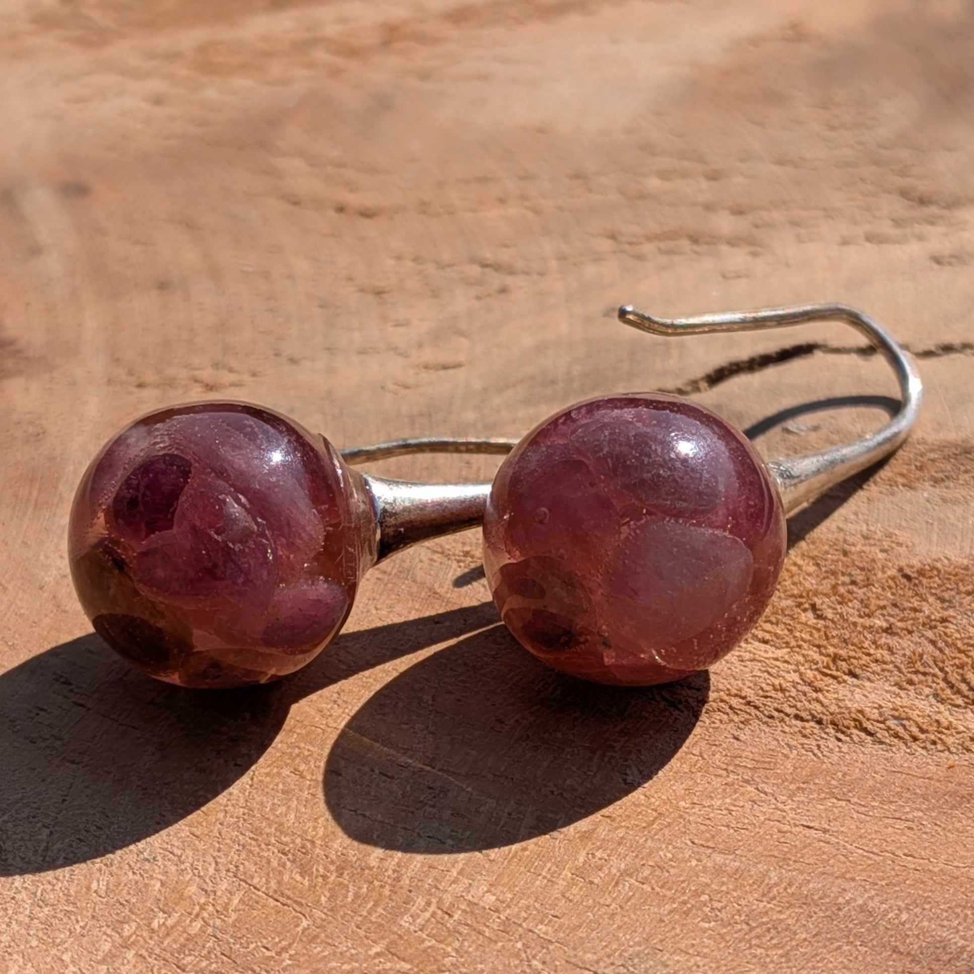 Pair of earrings with round, pinkish-red gemstones on a wooden surface