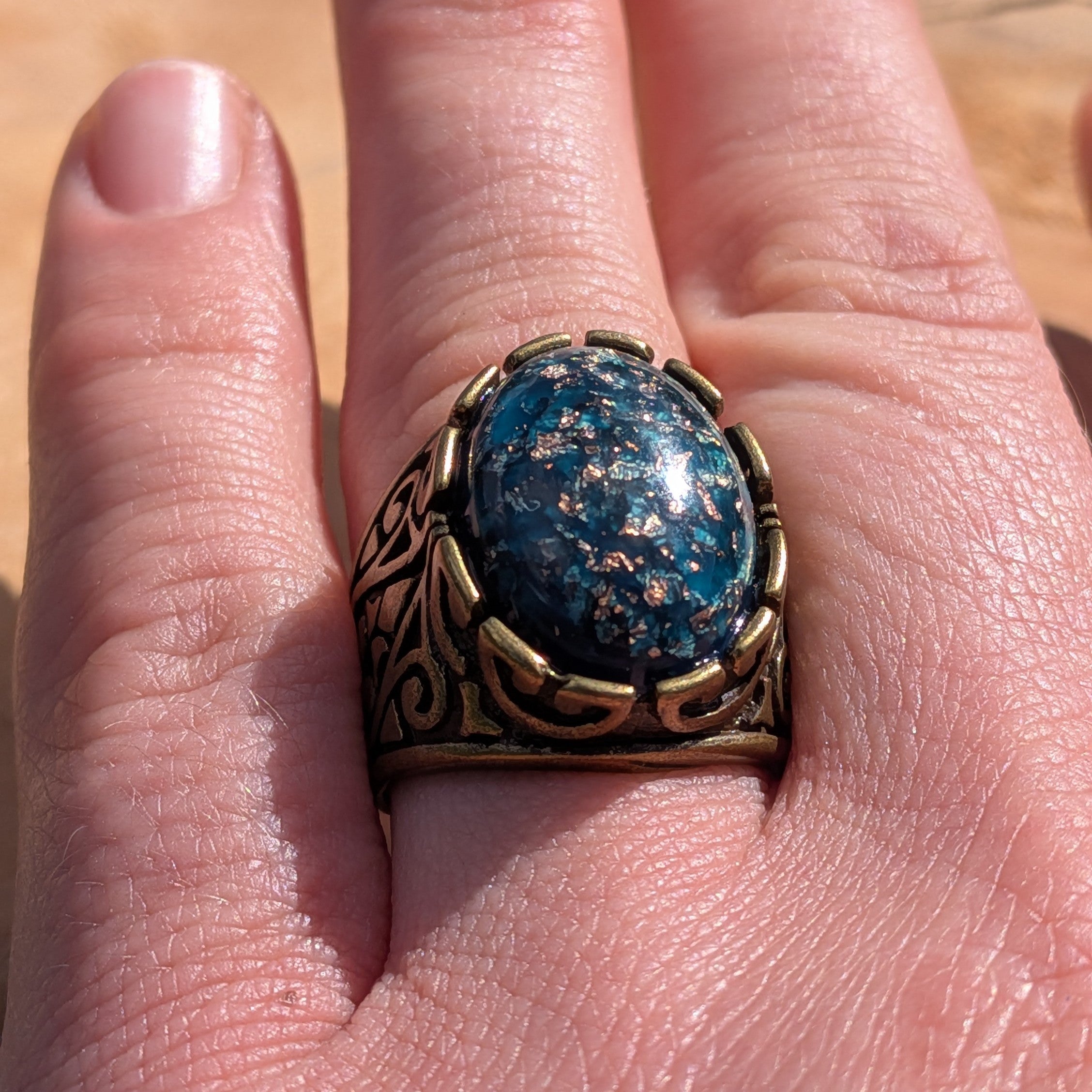 Teal blue resin ring antique bronze filigree claw setting worn on finger side view in sunlight – EL-Creations