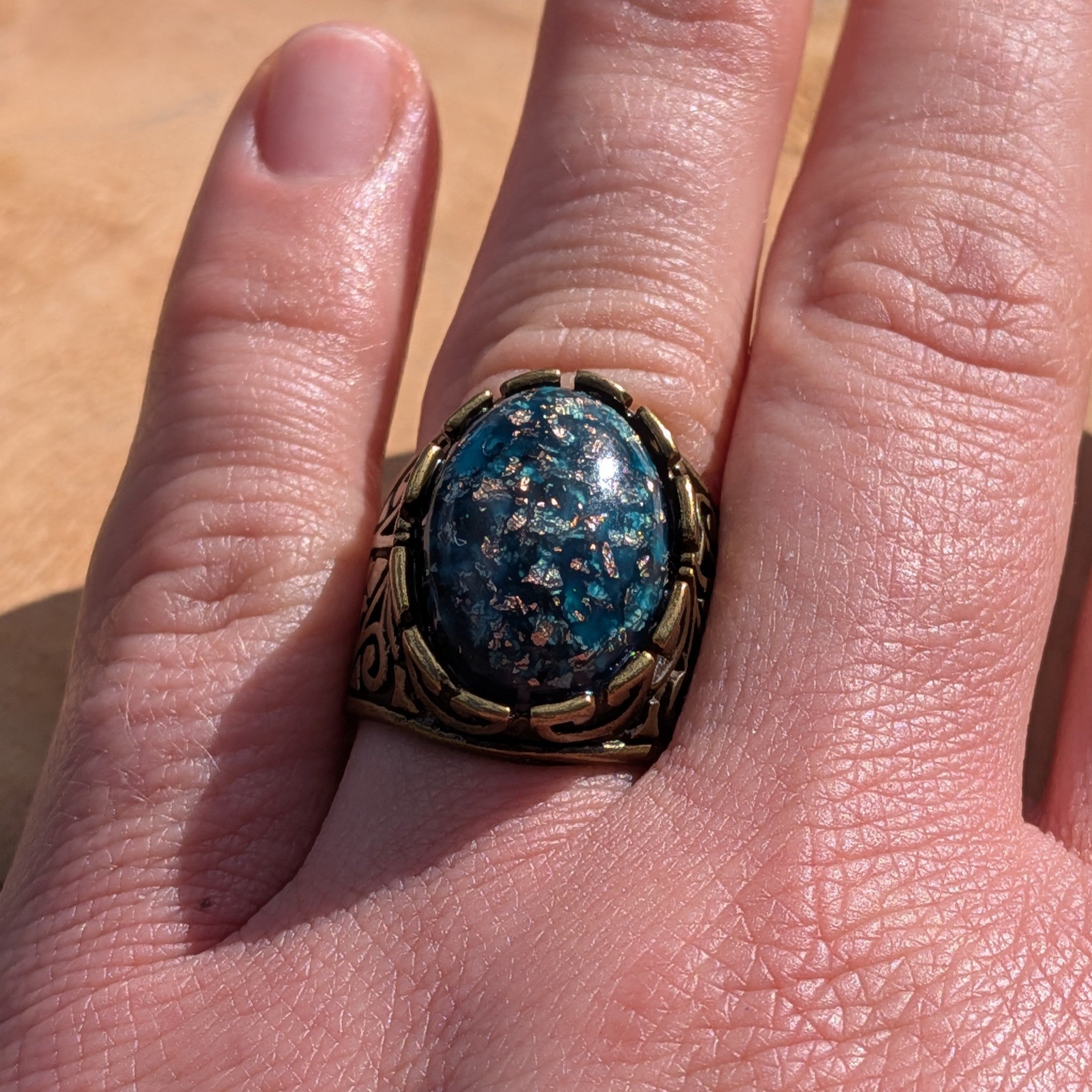 Teal blue resin ring antique bronze scrollwork band worn on finger top view copper flakes – EL-Creations