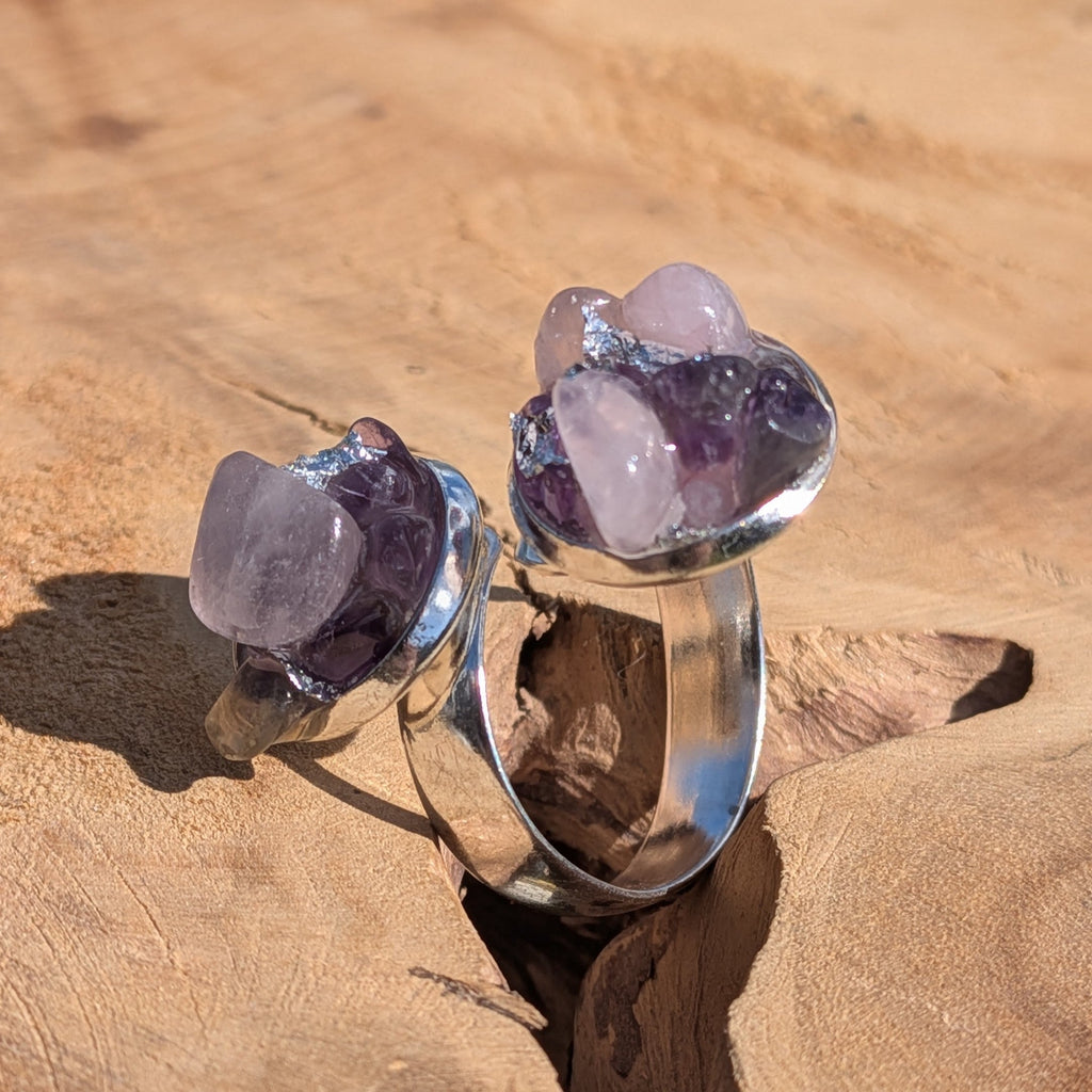 Two amethyst rose quartz bypass rings on sandy wood, angled view of dual crystal cluster settings – EL-Creations