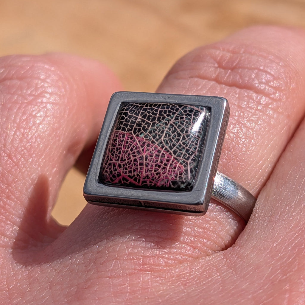 Black burgundy skeleton leaf resin ring worn on finger, close-up of square stainless steel bezel – EL-Creations