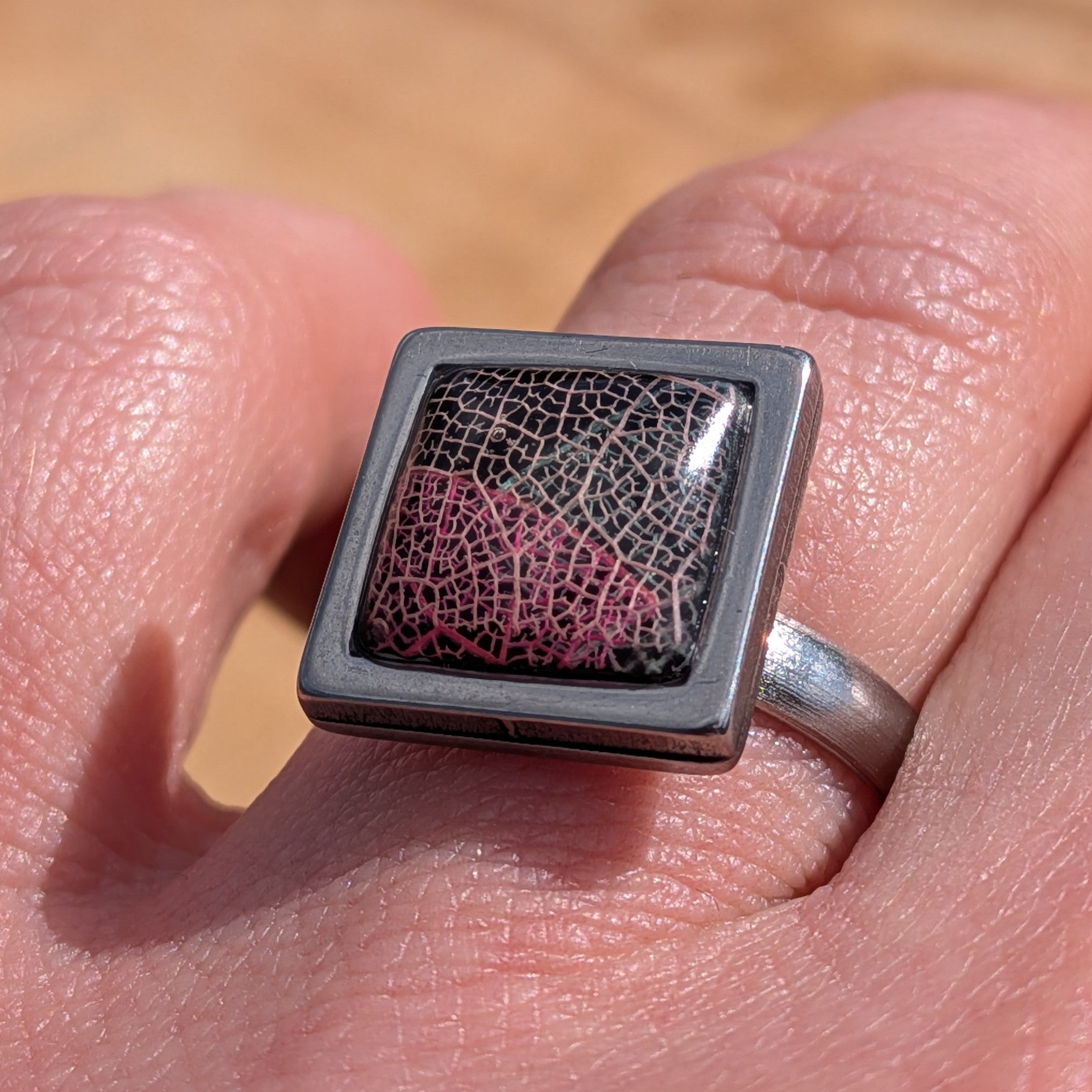 Black burgundy skeleton leaf resin ring worn on finger, close-up of square stainless steel bezel – EL-Creations