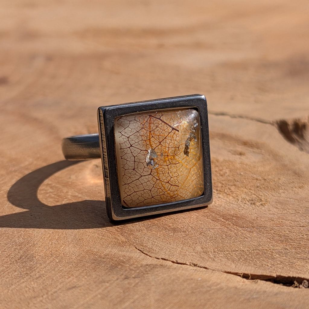 Side view of skeleton leaf resin ring on wood, clear resin dome with copper gold flakes in square stainless steel setting – EL-Creations