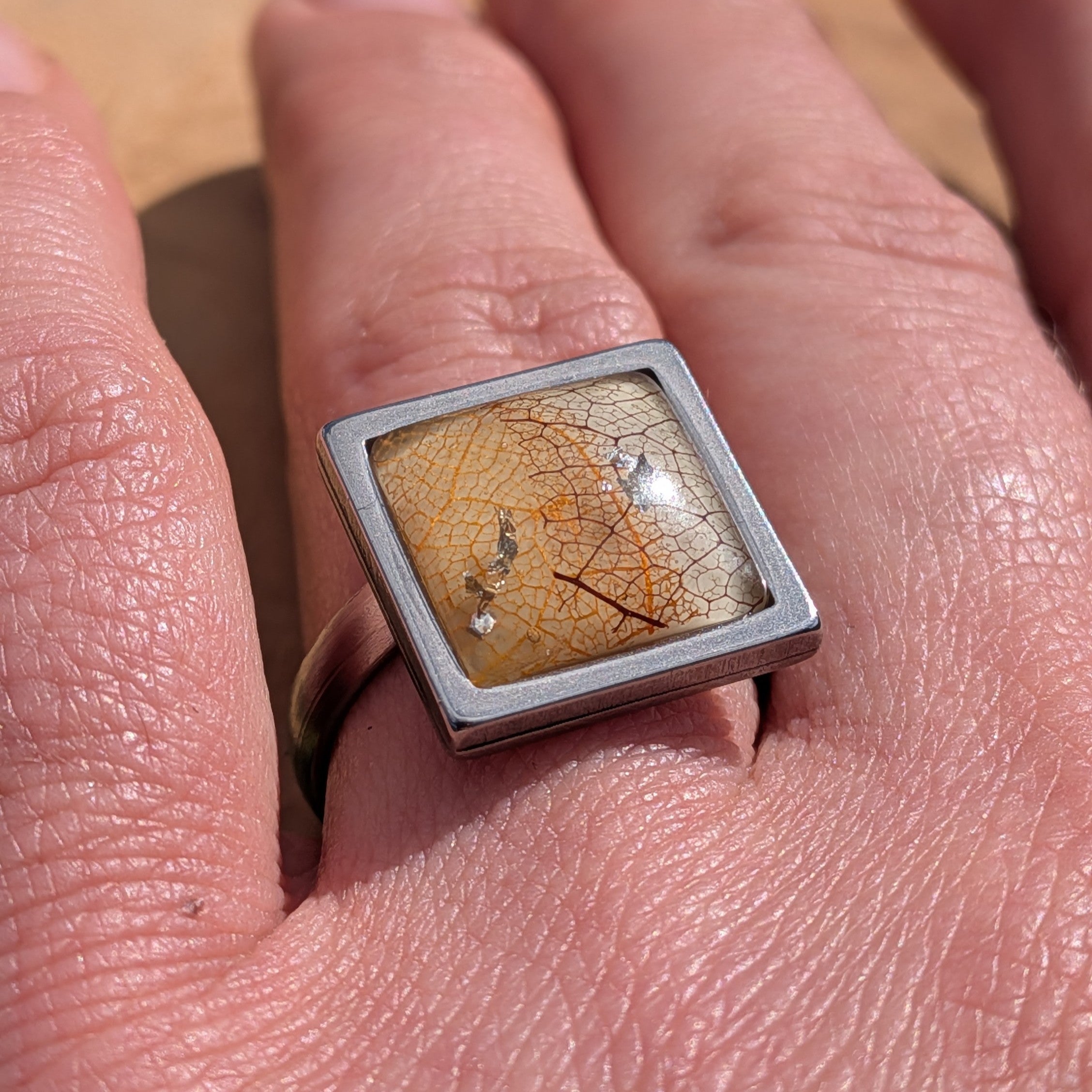 Skeleton leaf resin ring on wood, angled view showing gunmetal stainless steel band and square bezel – EL-Creations