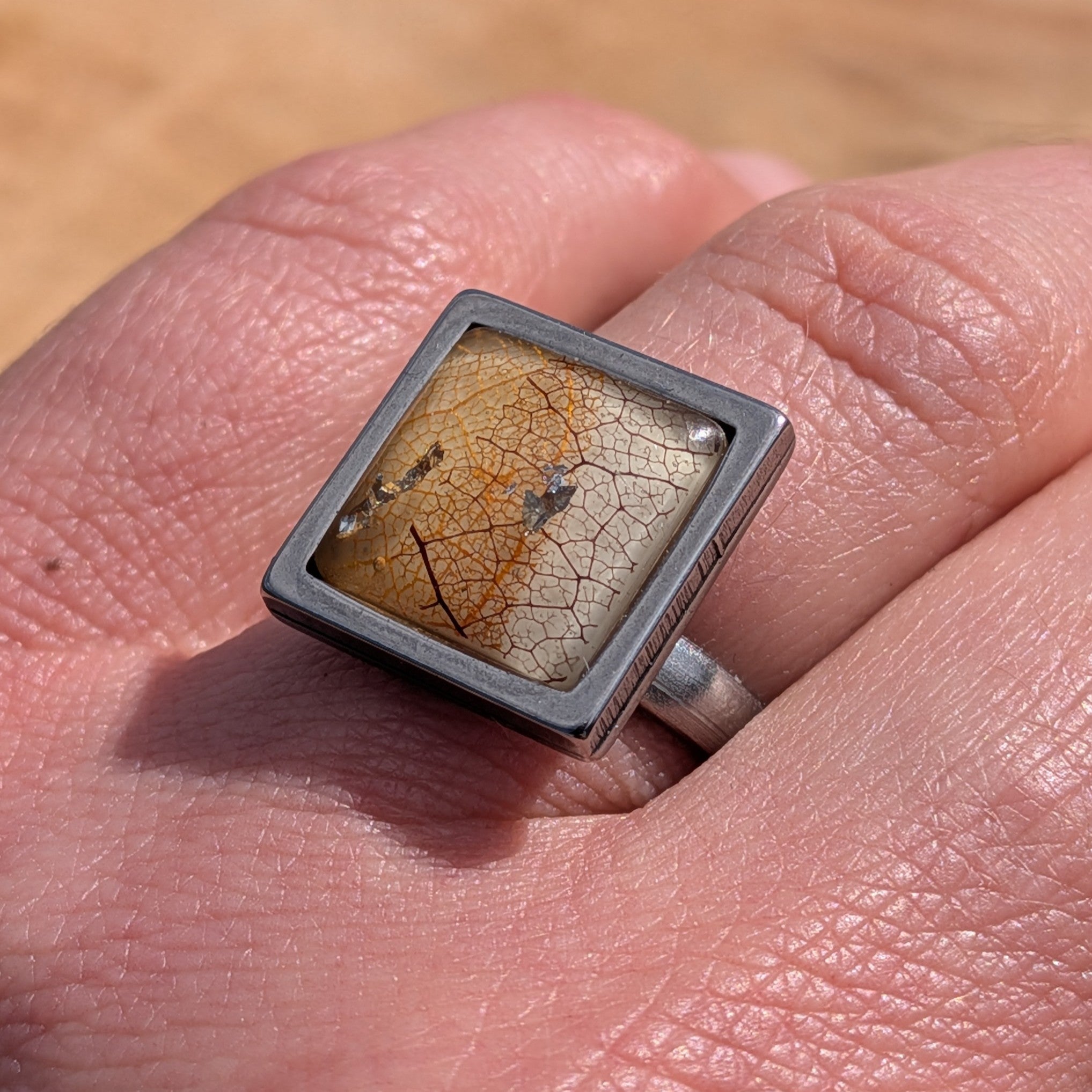 Skeleton leaf resin ring worn on finger, close-up of 15mm square stainless steel bezel with copper gold flakes – EL-Creations