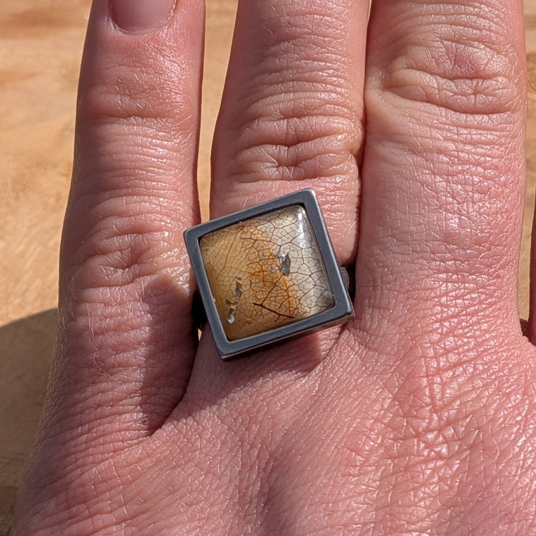 Handcrafted skeleton leaf resin ring on hand, square gunmetal stainless steel setting with amber leaf and metallic flakes – EL-Creations