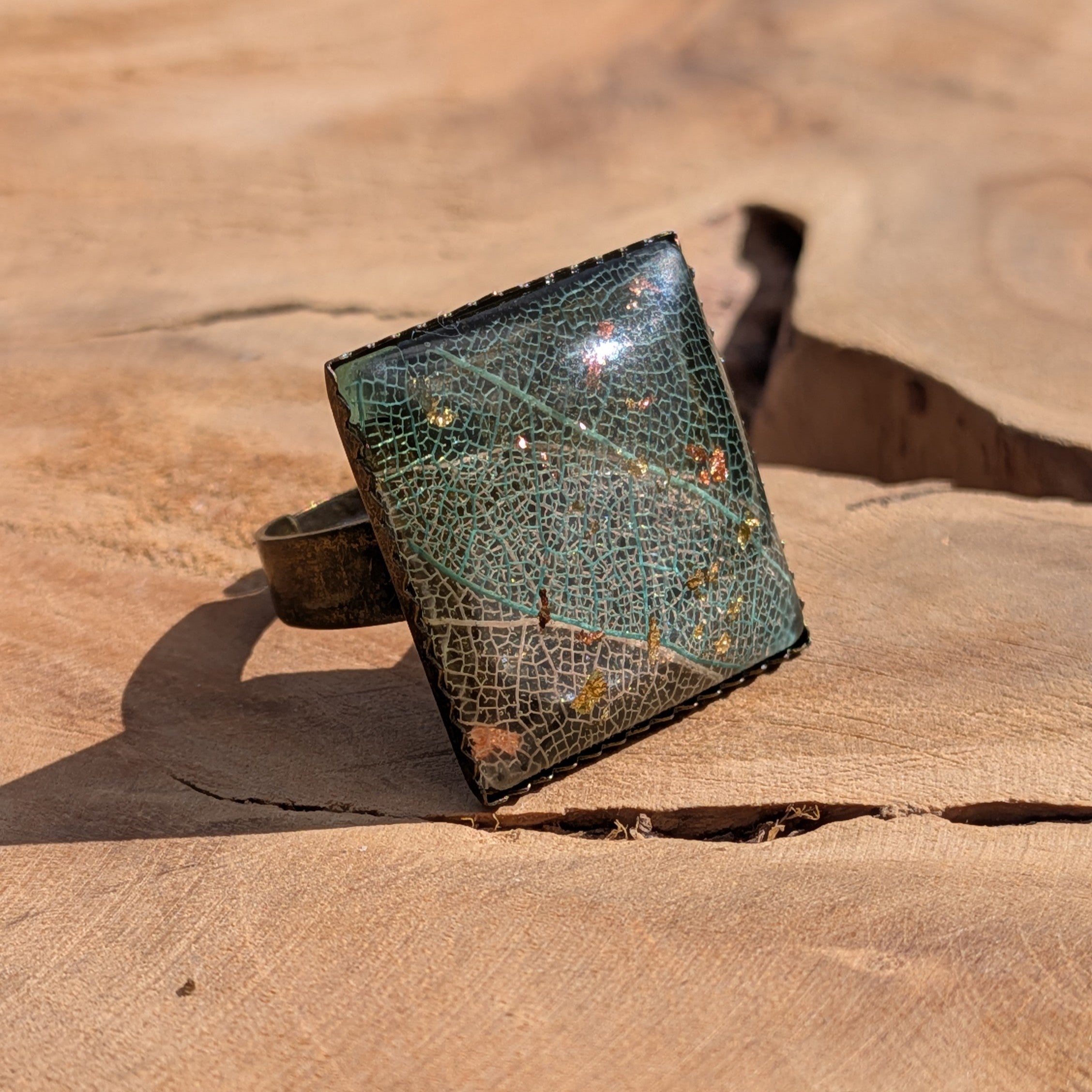 Top view of skeleton leaf resin ring on wood, copper and gold flakes in dark resin square bronze setting – EL-Creations