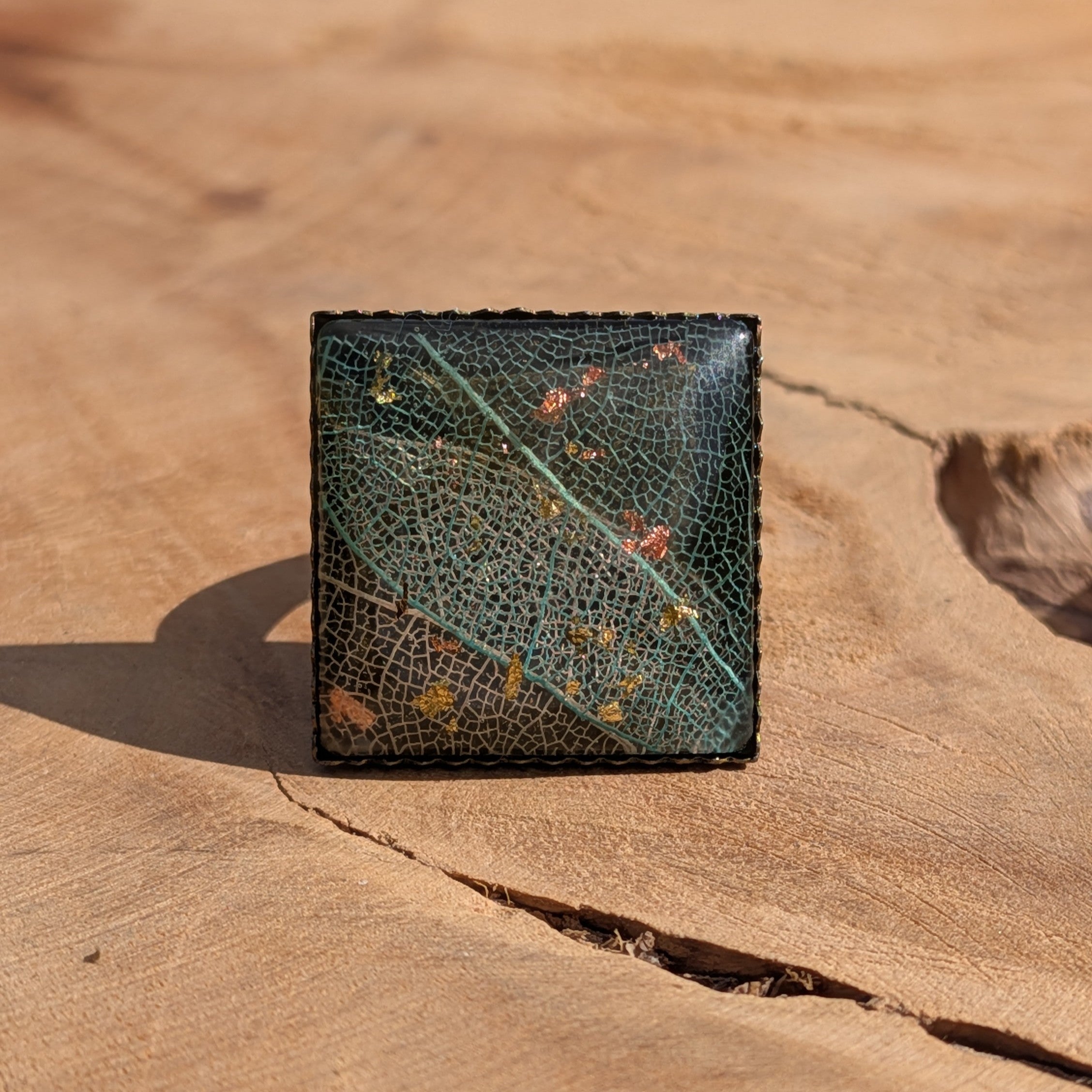 Front view of skeleton leaf resin ring on wood, 20×20mm square antique bronze bezel with decorative edge – EL-Creations