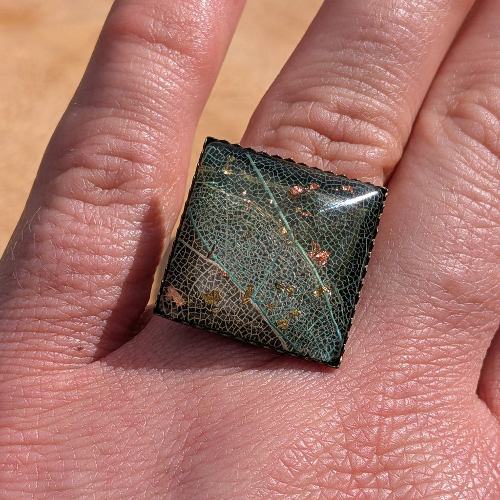 Side view of skeleton leaf resin ring on wood, dark resin dome with copper gold flakes in bronze setting – EL-Creations