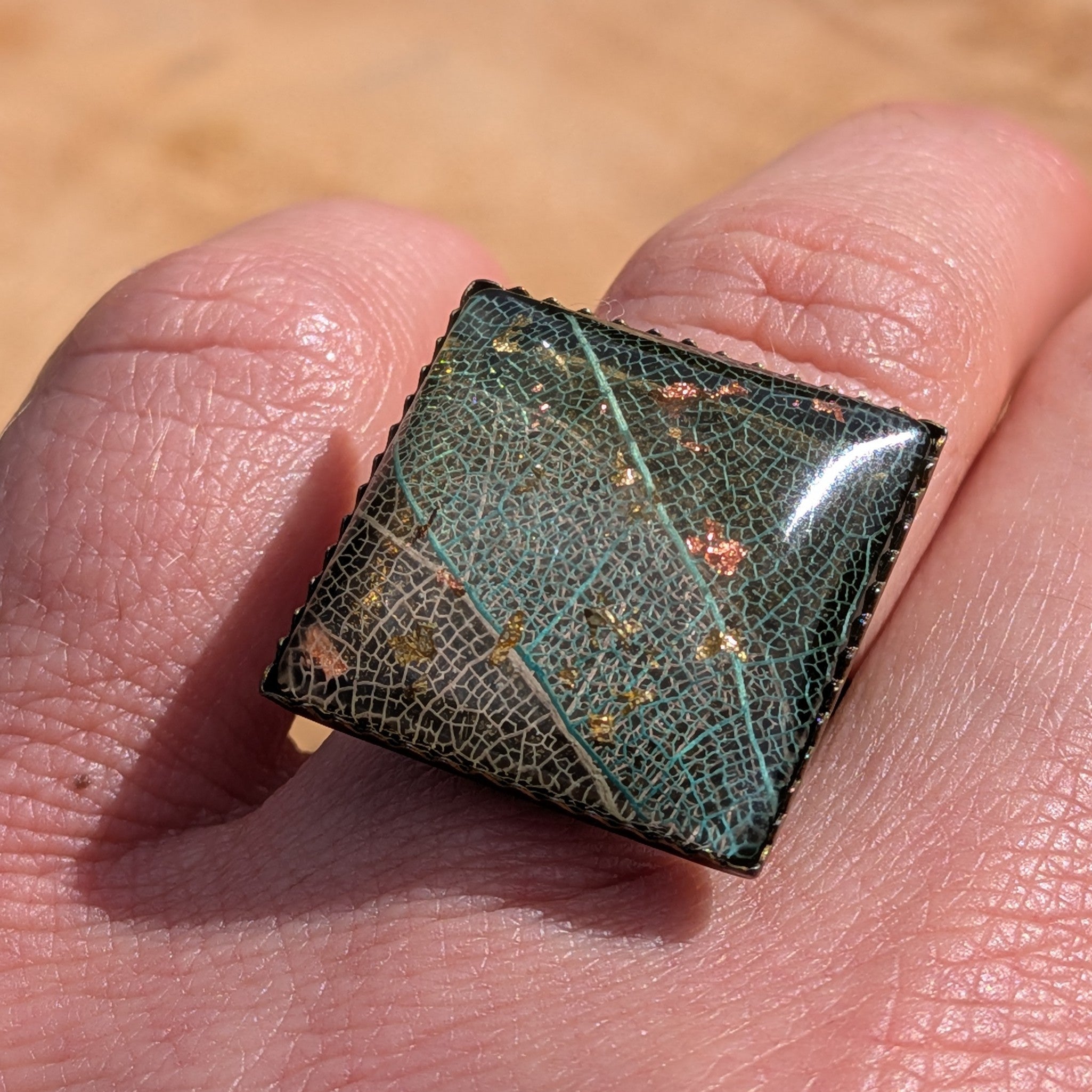 Skeleton leaf resin ring on wood, angled view of 20mm square bronze bezel with copper and gold flakes – EL-Creations
