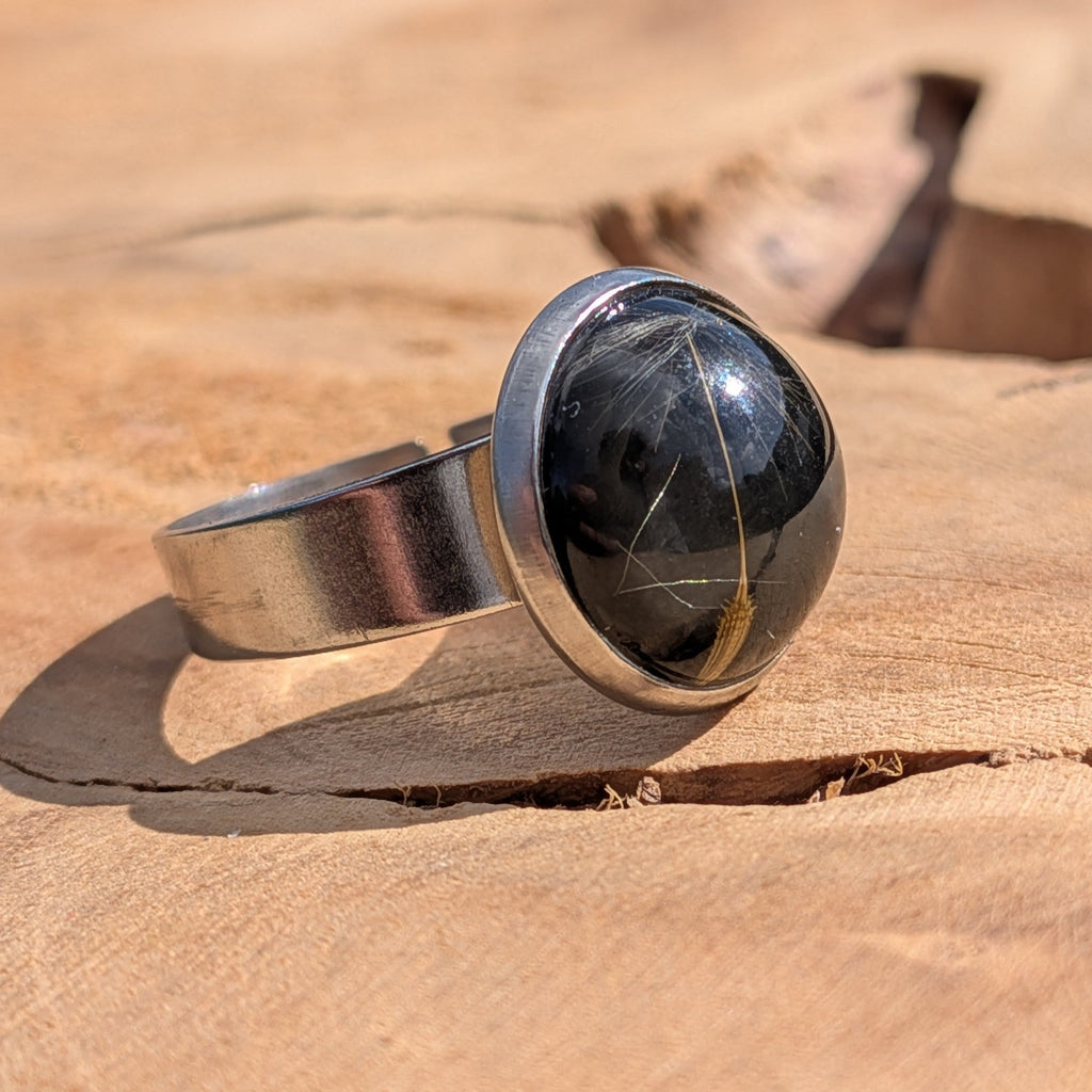 Top view of black dandelion resin ring on wood, real dandelion seeds in round stainless steel bezel – EL-Creations