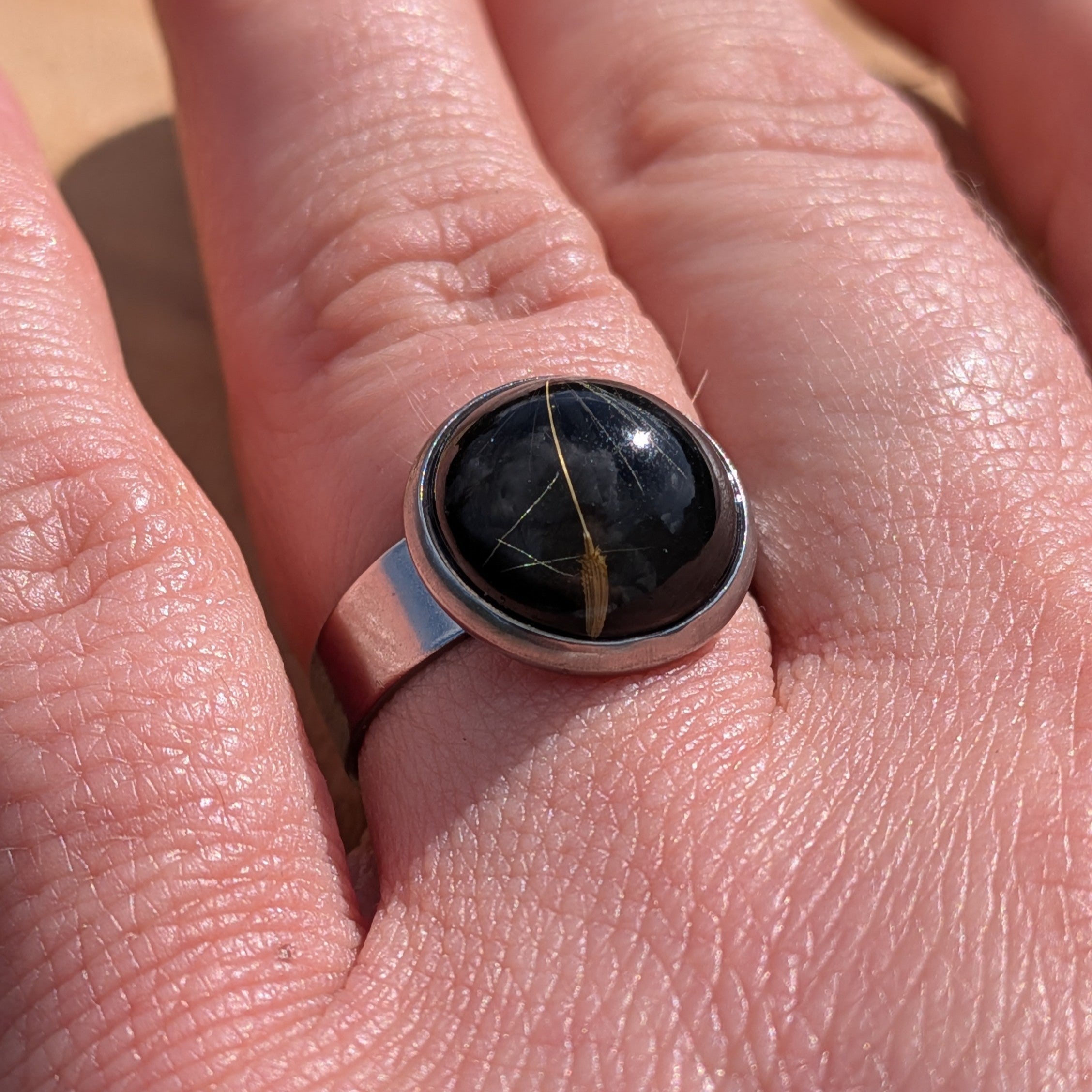 Black dandelion resin ring on finger, angled view of round stainless steel bezel with gloss dome – EL-Creations