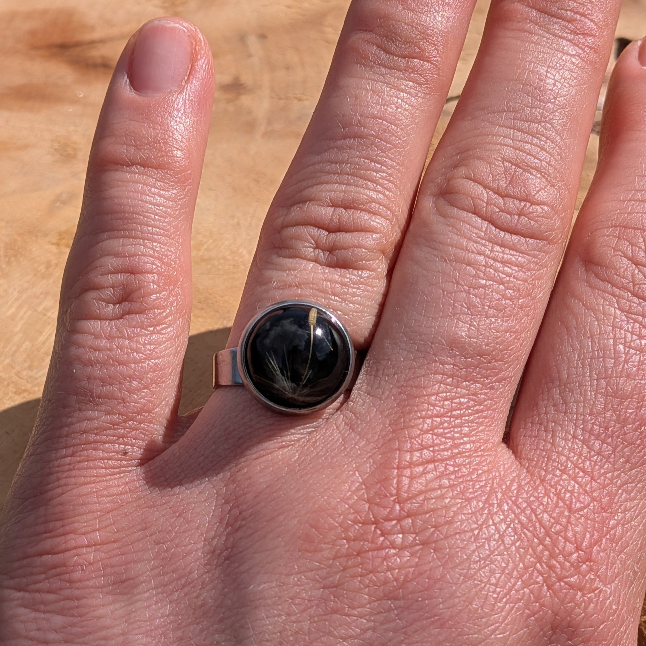 Black resin ring with real dandelion seeds worn on finger, wide stainless steel band – EL-Creations