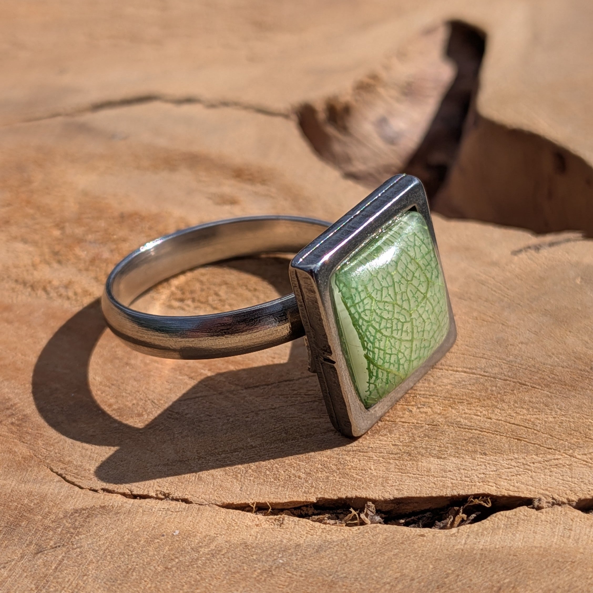 Side view of green skeleton leaf resin ring on wood, 14×14mm square steel bezel with gloss dome – EL-Creations