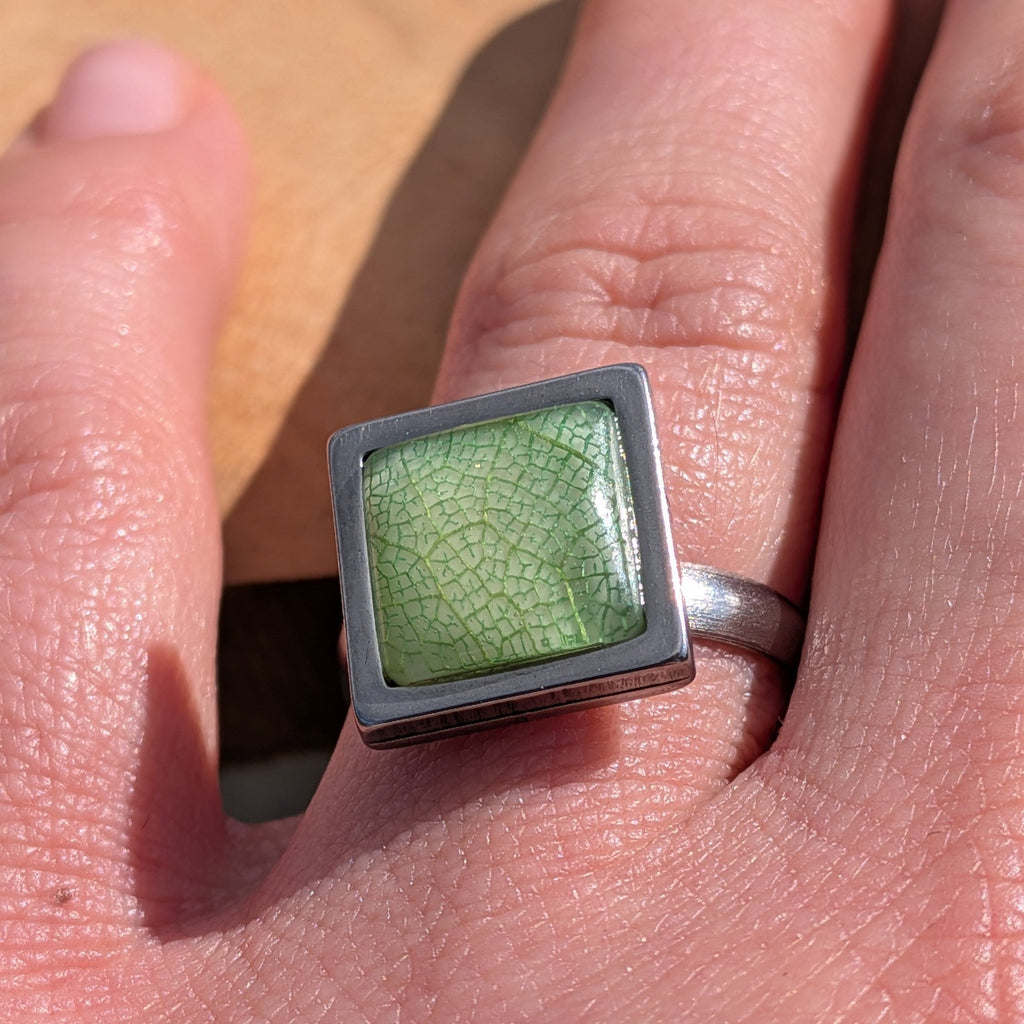 Green skeleton leaf resin ring worn on finger, close-up of square stainless steel bezel – EL-Creations