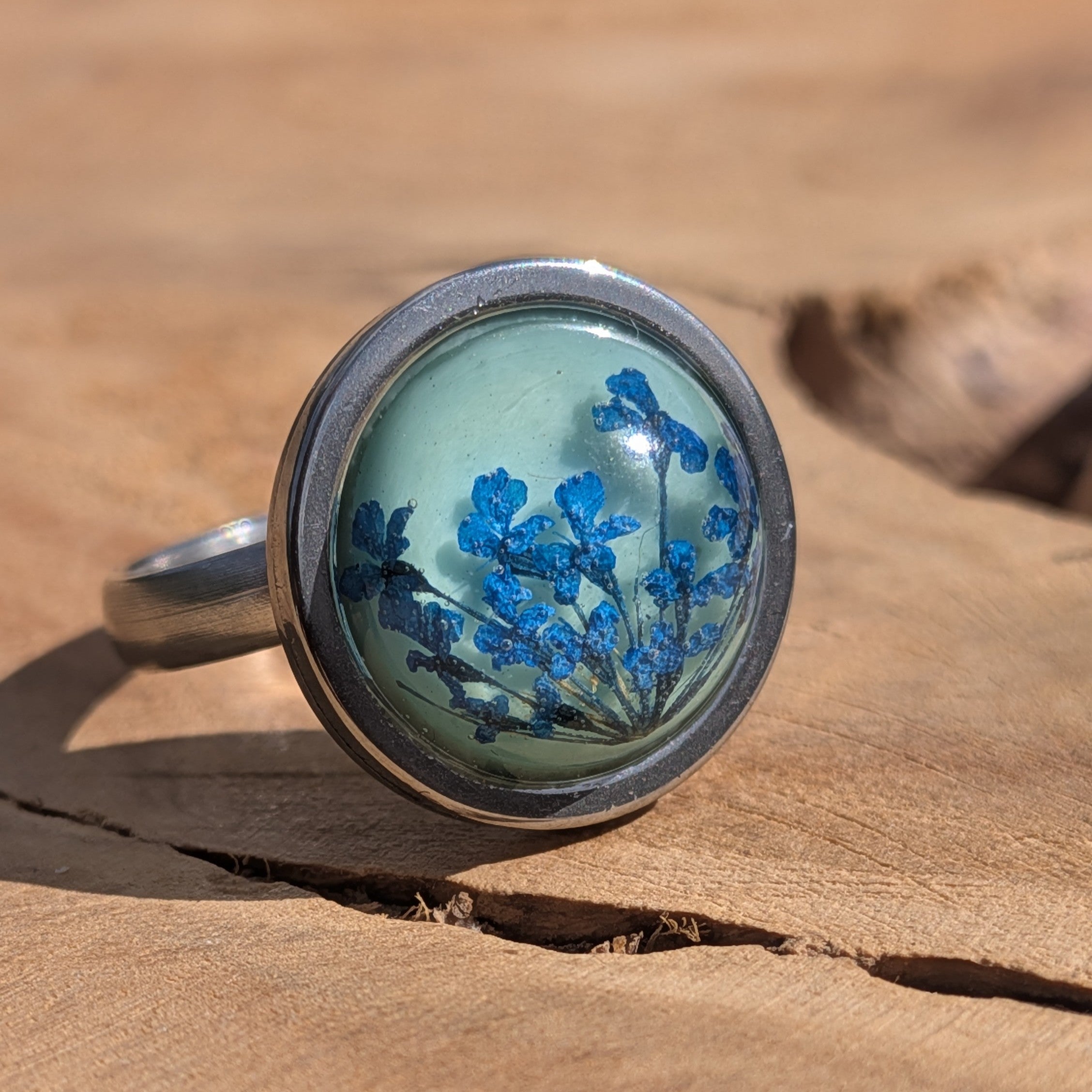 Close-up of blue floral resin ring on wood, dried flowers on teal base in stainless steel setting – EL-Creations