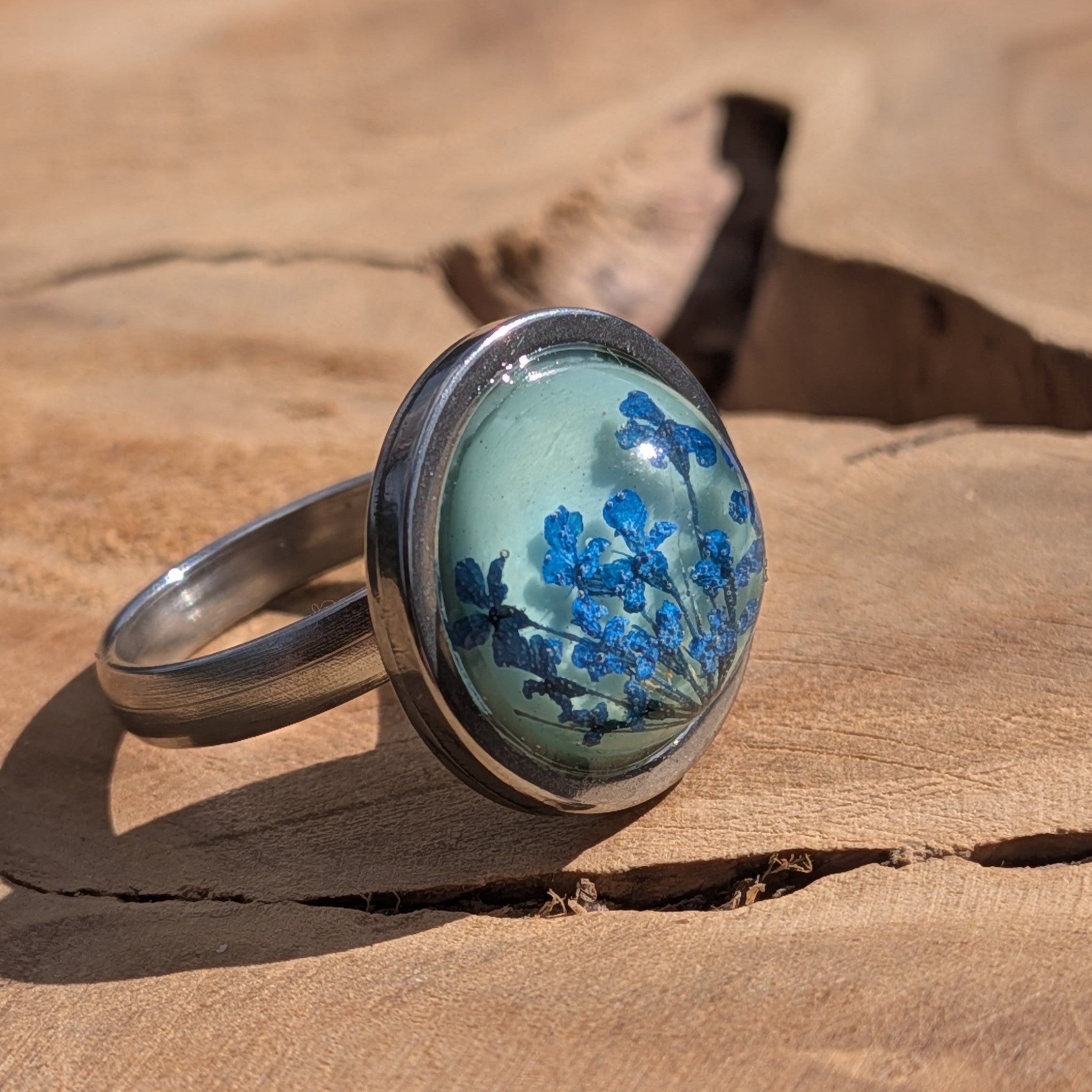 Side view of blue Queen Anne's Lace resin ring on wood, 16mm teal dome in stainless steel bezel – EL-Creations