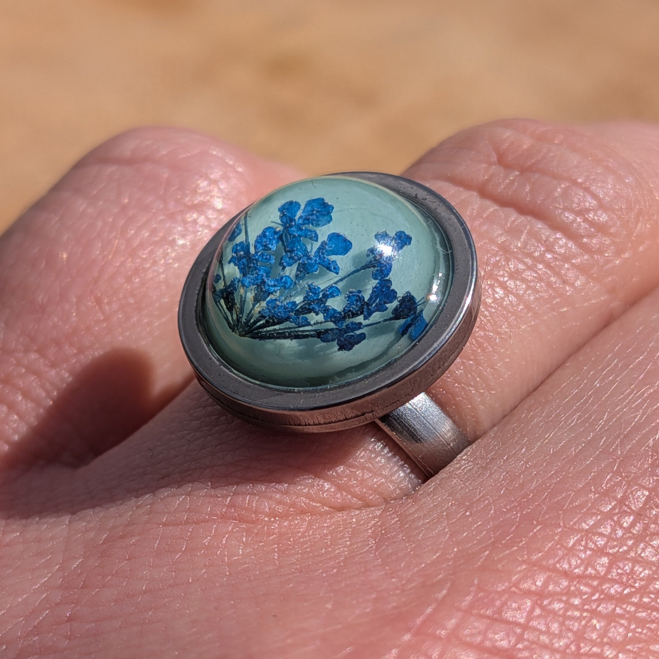 Blue Queen Anne's Lace ring on hand, top view of 16mm teal resin dome in stainless steel round setting – EL-Creations