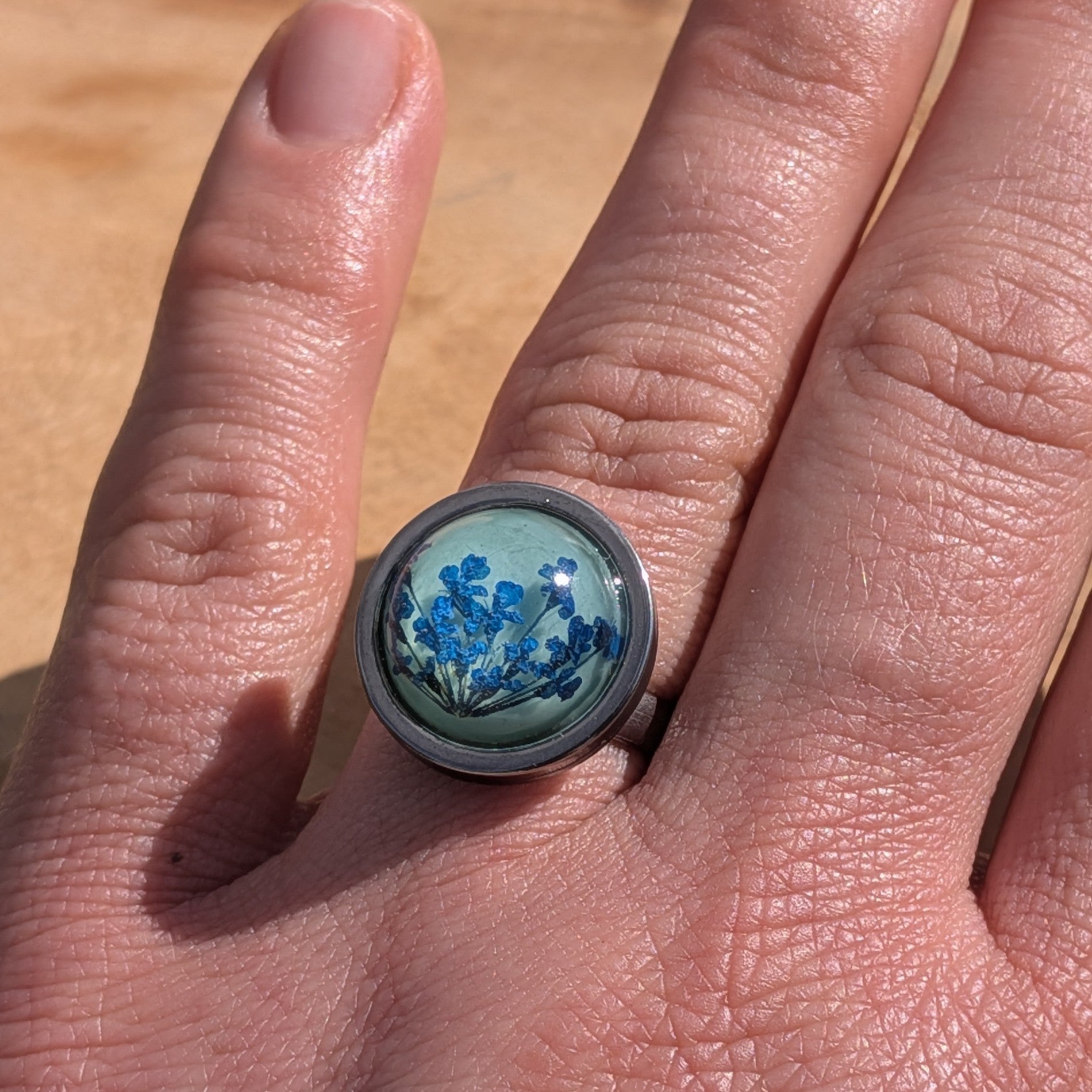 Handcrafted blue floral resin ring worn on finger, side view of teal cabochon in stainless steel bezel – EL-Creations