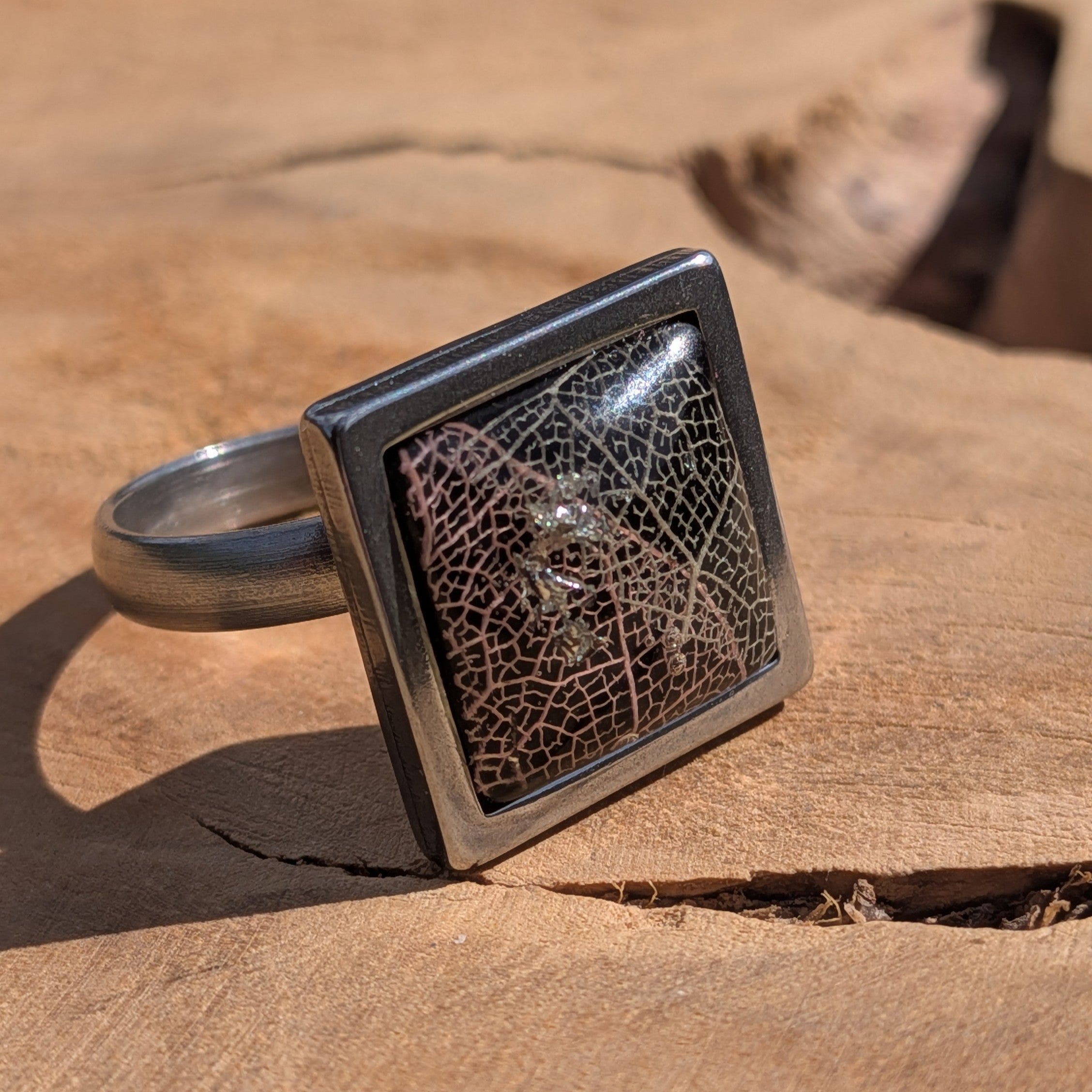 Side view of black botanical resin ring on wood, skeleton leaf in square stainless steel setting – EL-Creations
