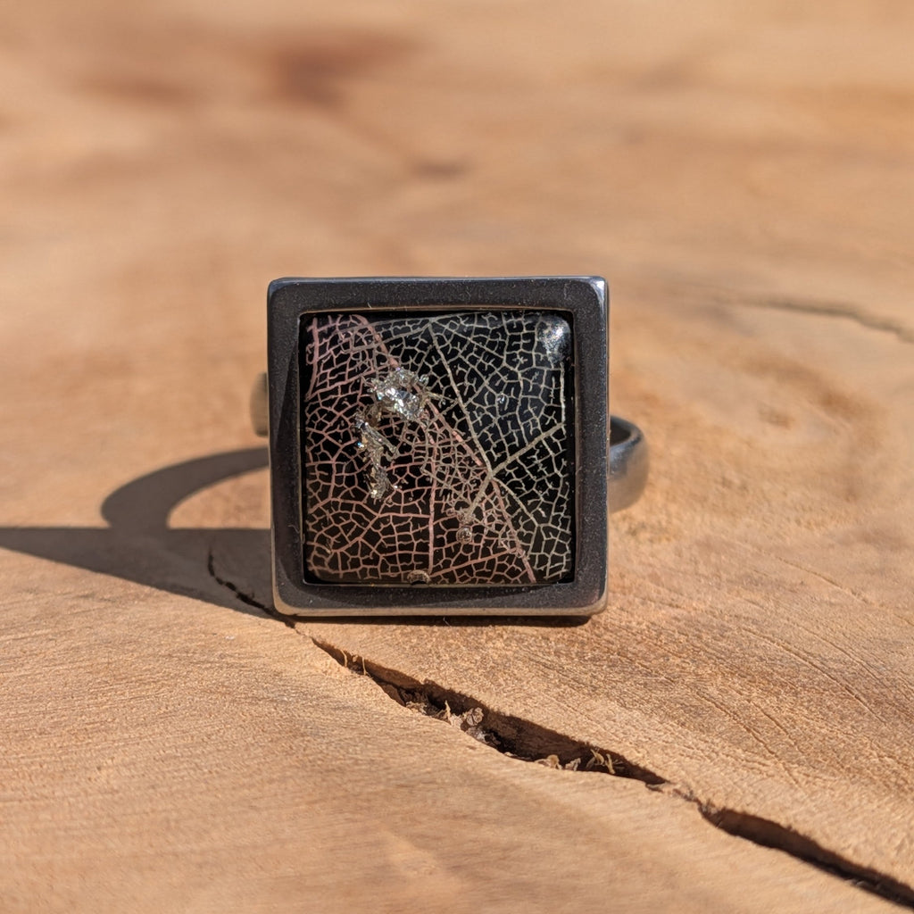 Black skeleton leaf resin ring worn on finger, close-up of square stainless steel bezel – EL-Creations