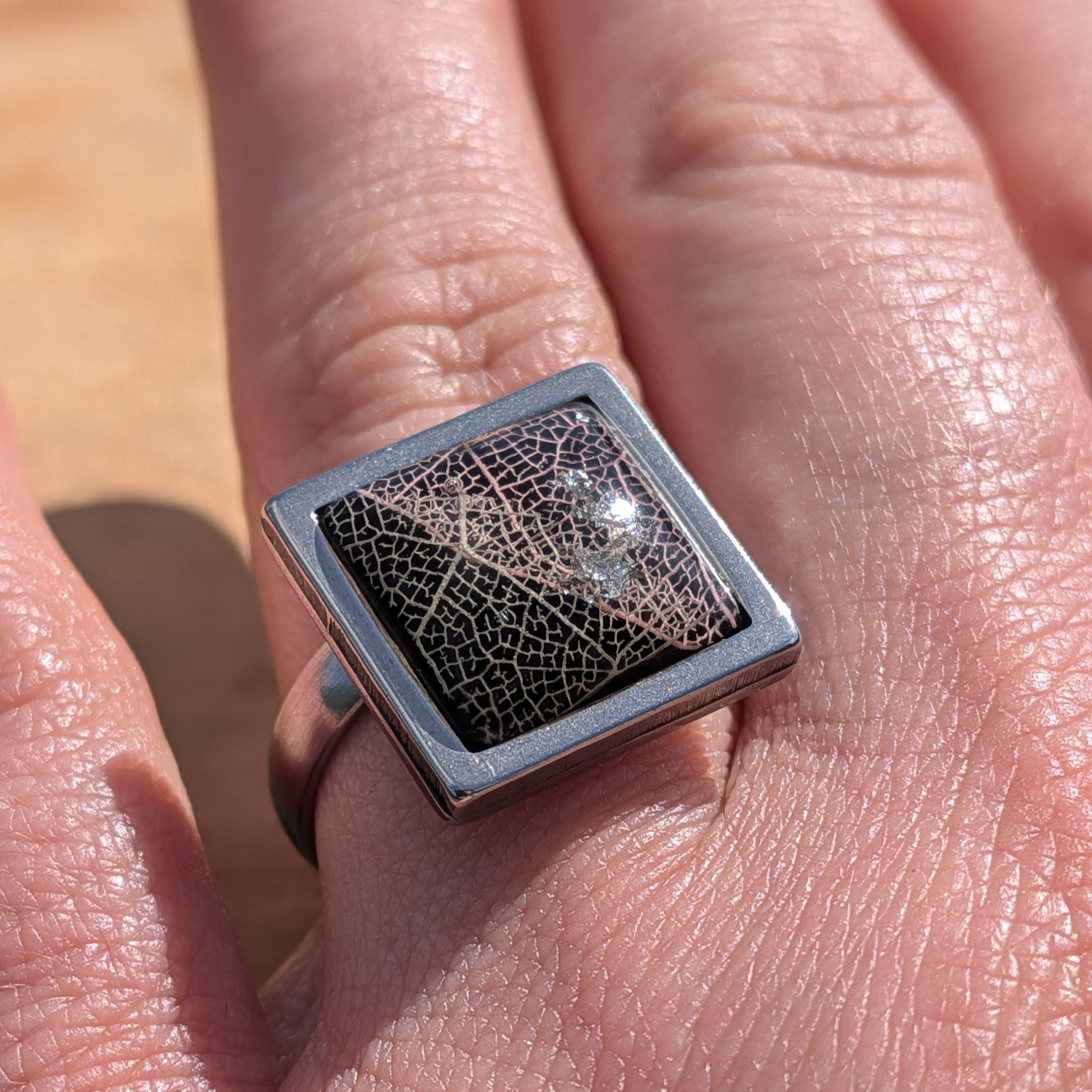 Black botanical resin ring worn on finger, angled view of square steel bezel with skeleton leaf – EL-Creations