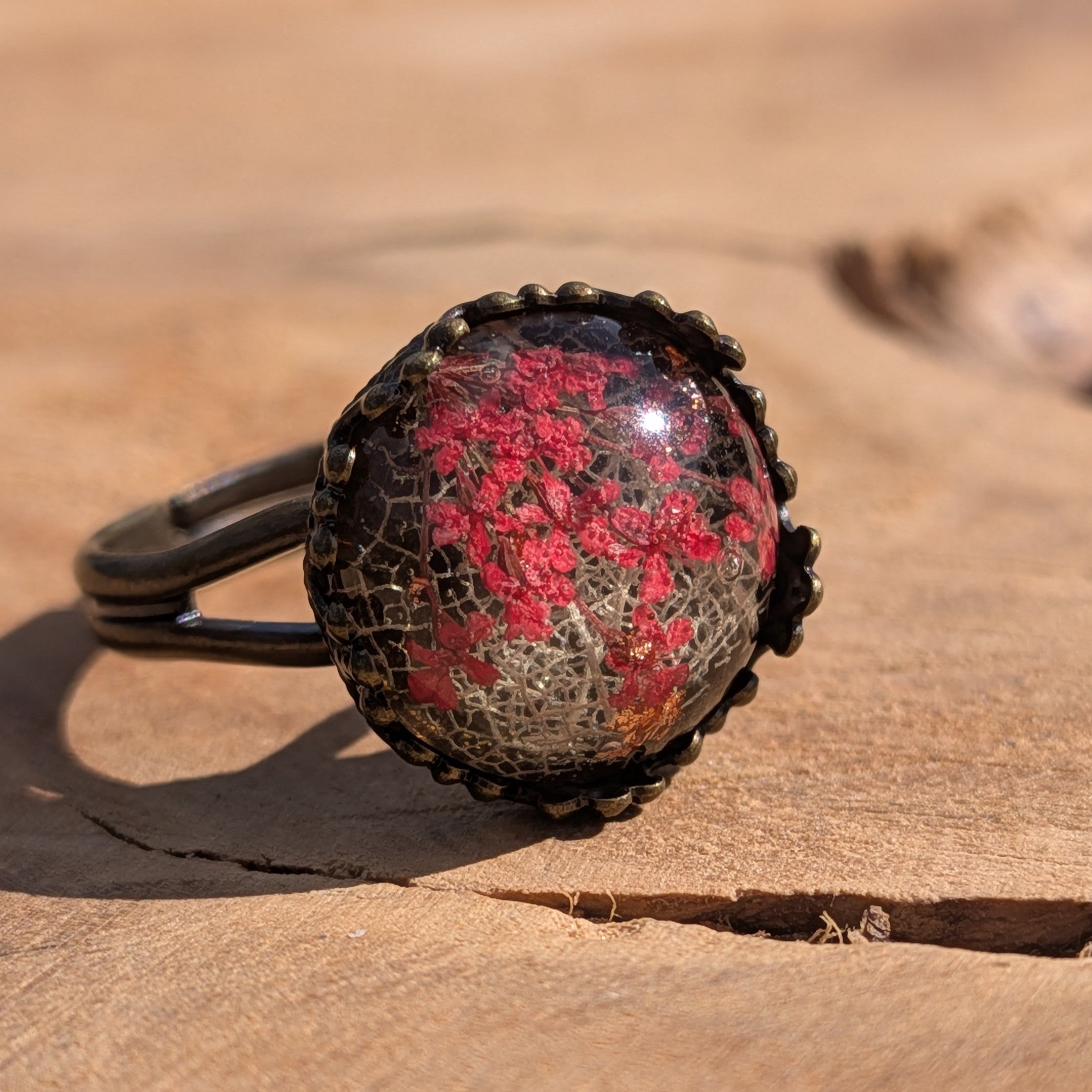 Side view of red botanical resin ring on wood, dried flowers and skeleton leaf in bronze crown bezel – EL-Creations