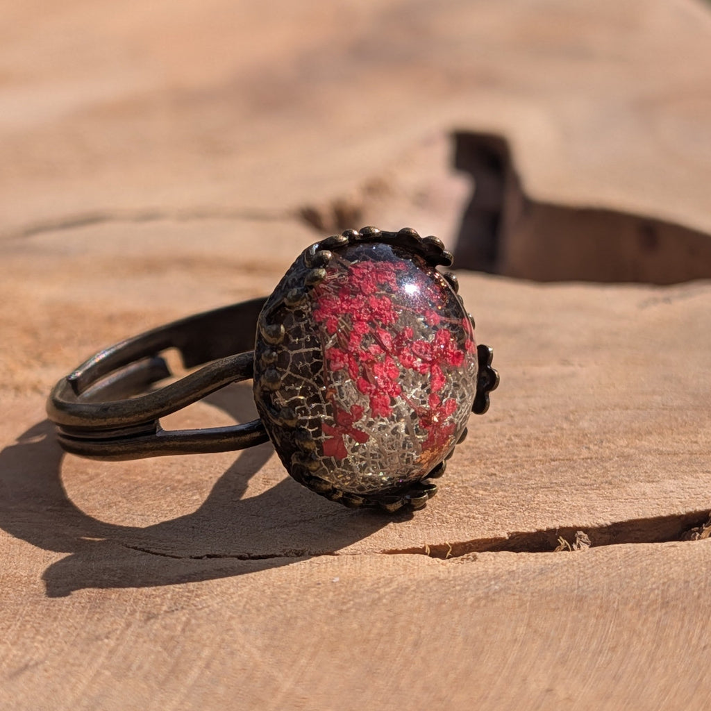 Red floral resin ring on wooden surface, angled view of 13mm cabochon with Queen Anne's Lace in bronze setting – EL-Creations