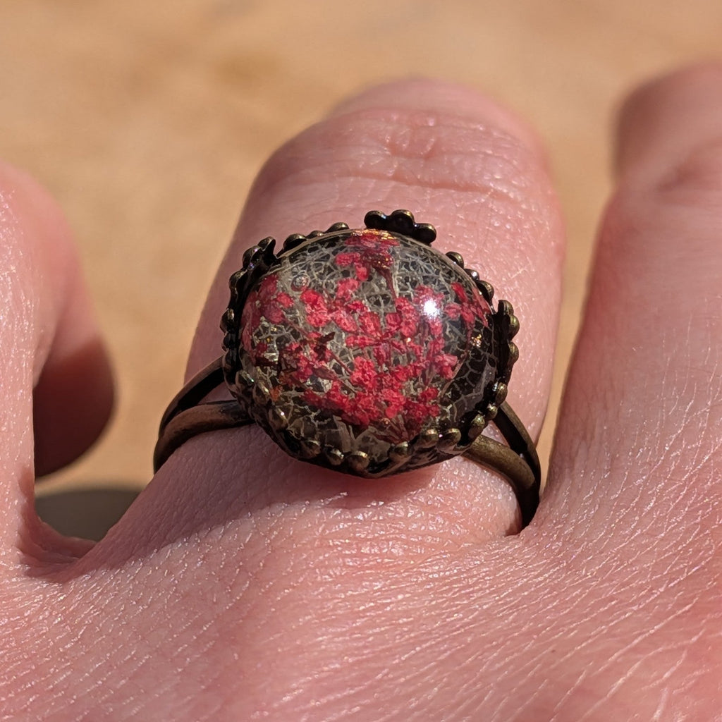 Red dried flower resin ring worn on finger, side view of 13mm dome cabochon in ornate bronze crown setting – EL-Creations