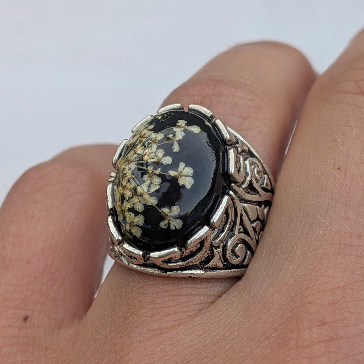 Black botanical resin statement ring 18x15mm oval cabochon side view on wooden surface – EL-Creations