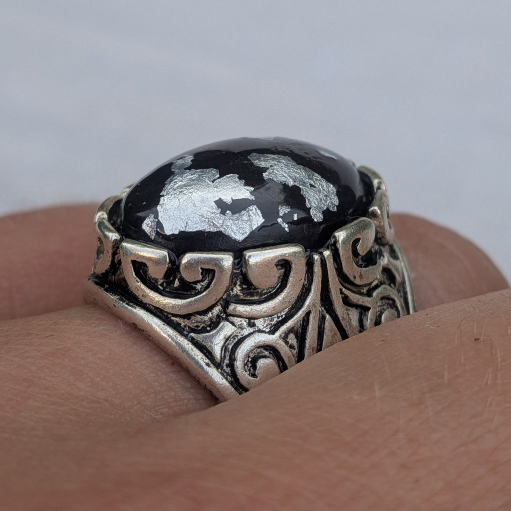 Oval black resin ring with silver flakes angled view ornate antique silver band on wood – EL-Creations