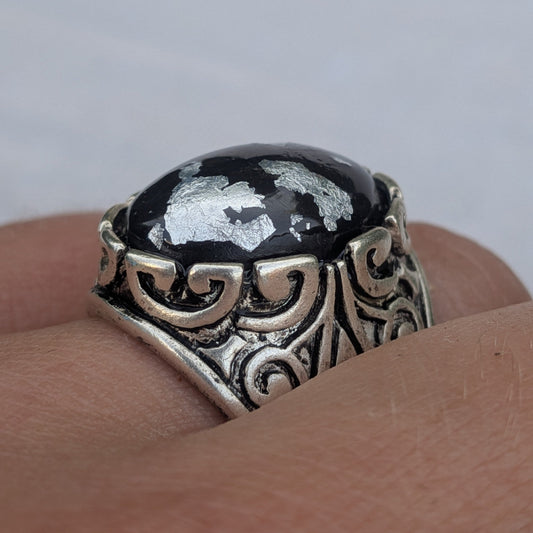 Oval black resin ring with silver flakes angled view ornate antique silver band on wood – EL-Creations