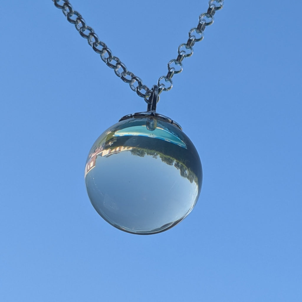 Transparent resin sphere necklace held up against blue sky — minimalist handcrafted jewelry
