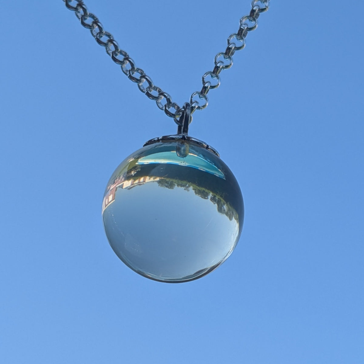 Transparent resin sphere necklace held up against blue sky — minimalist handcrafted jewelry