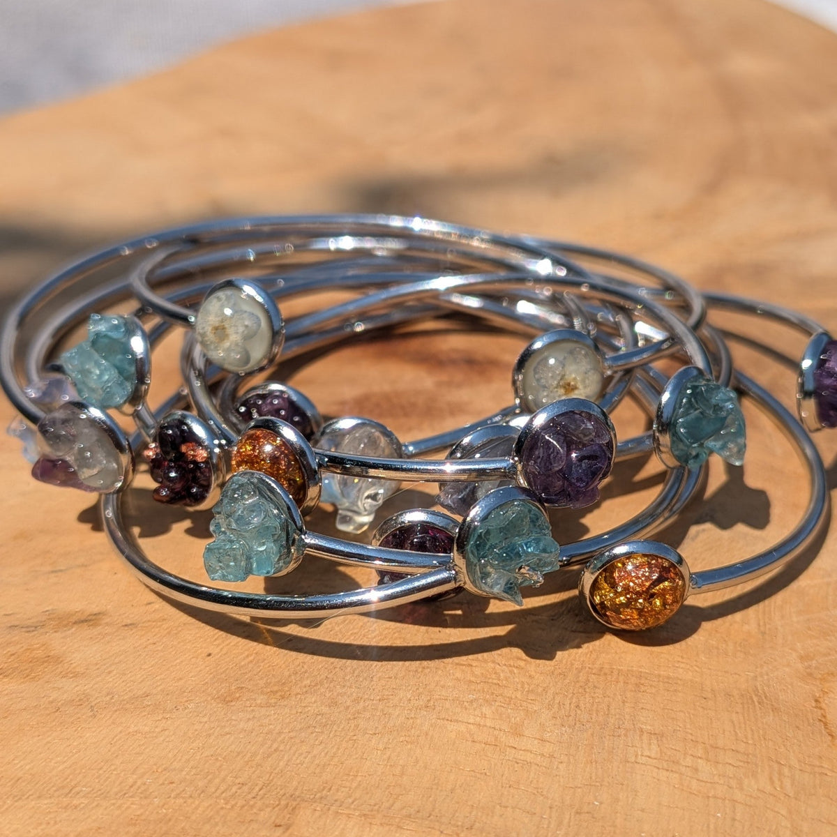 Collection of handmade crystal and flower resin cuff bracelets on wooden surface – EL-Creations