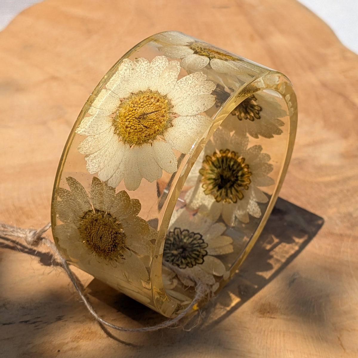 White daisy resin cuff bracelet resting on natural wood by EL-Creations