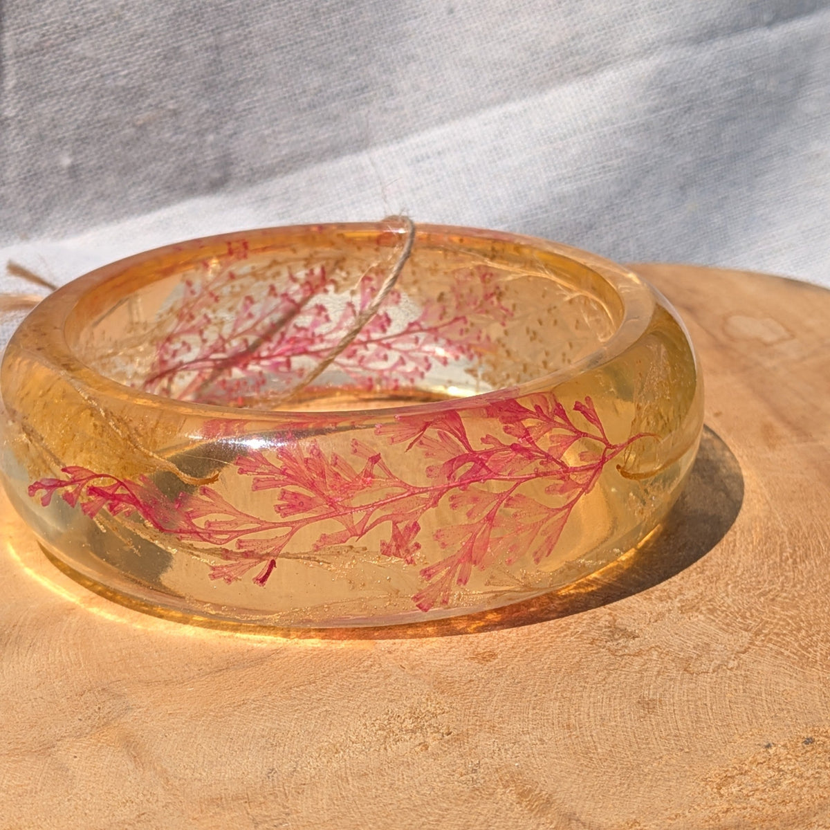 Close-up of red fern leaves and gold flakes inside amber resin bangle by EL-Creations