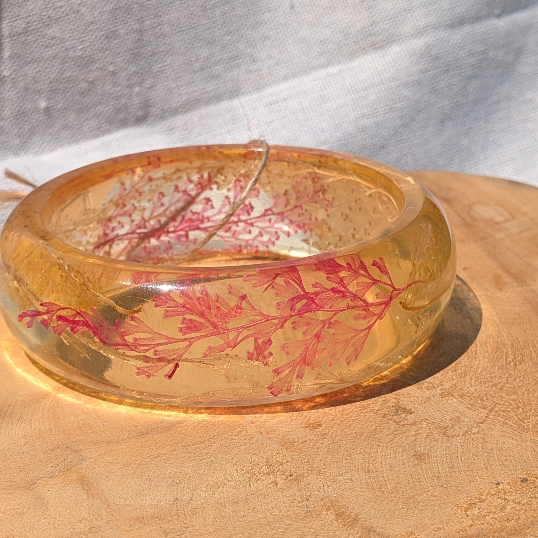 Close-up of red fern leaves and gold flakes inside amber resin bangle by EL-Creations