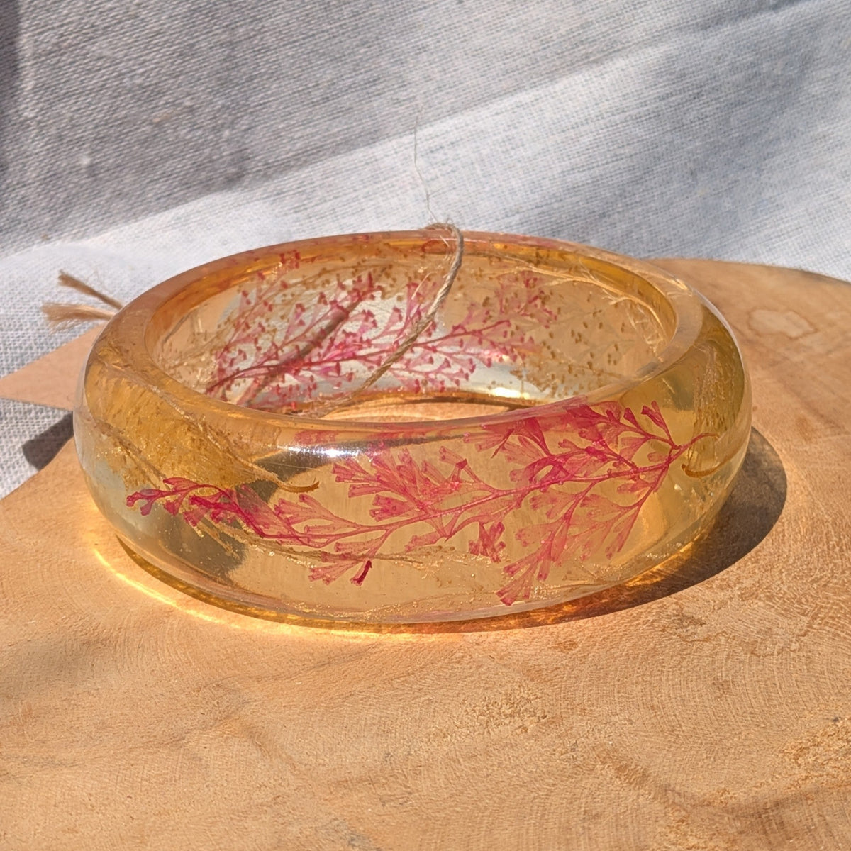 Top view of amber resin cuff with pressed red fern fronds on wood by EL-Creations