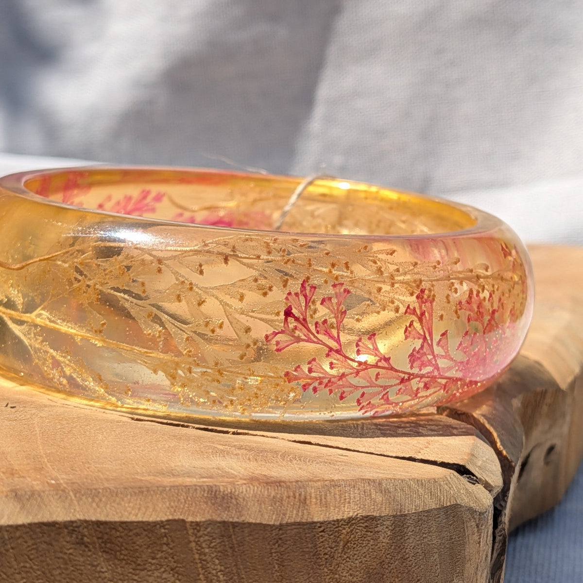 Wide amber resin bangle with red fern and gold flakes on wooden surface by EL-Creations