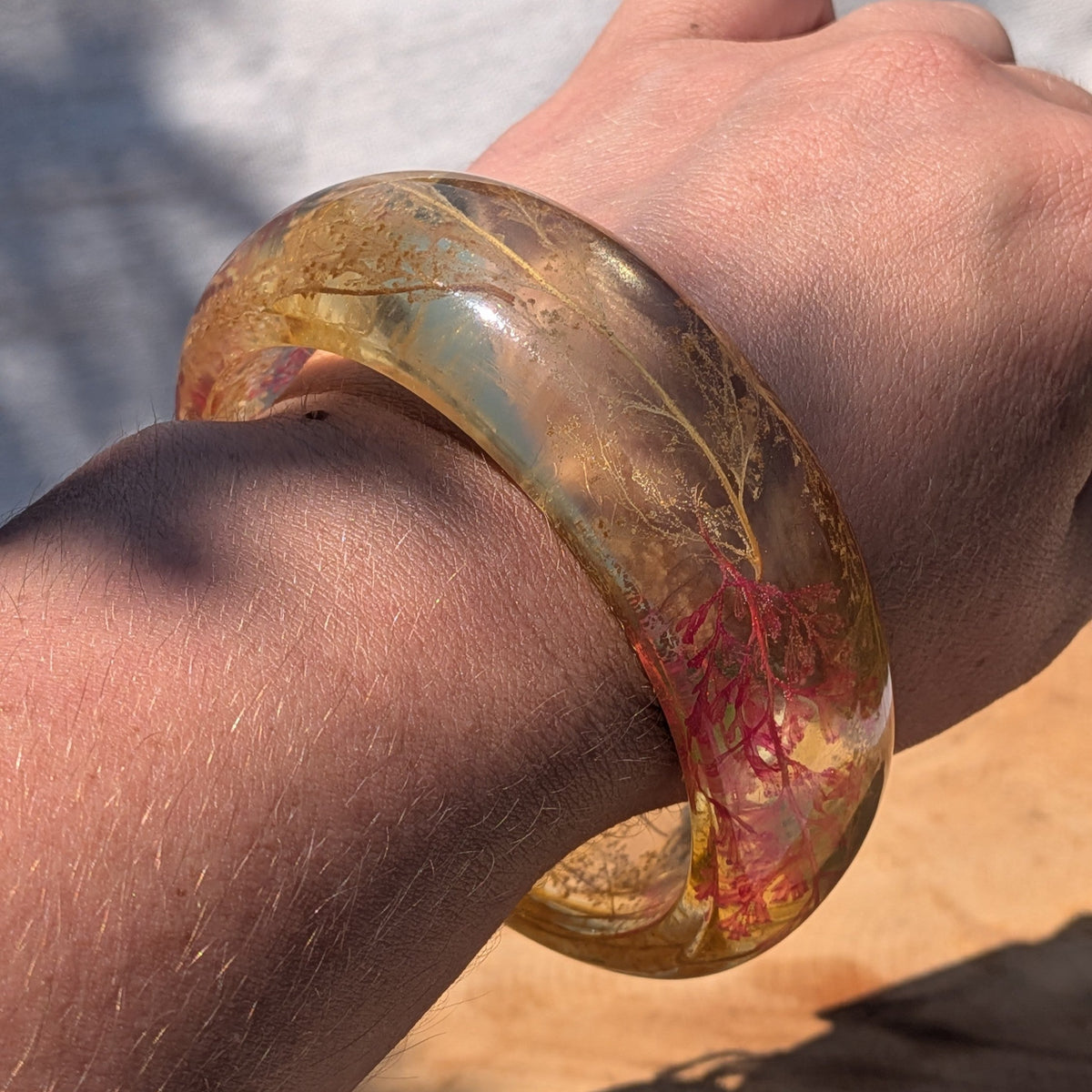 Luminous amber resin cuff bracelet with real botanical fern held to light by EL-Creations