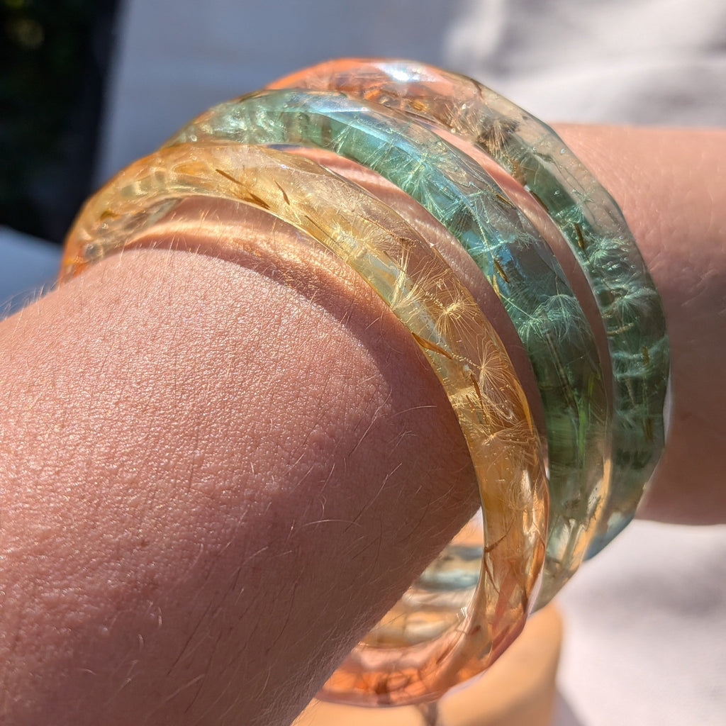 Stacked colourful dandelion seed resin bangles on natural wood by EL-Creations