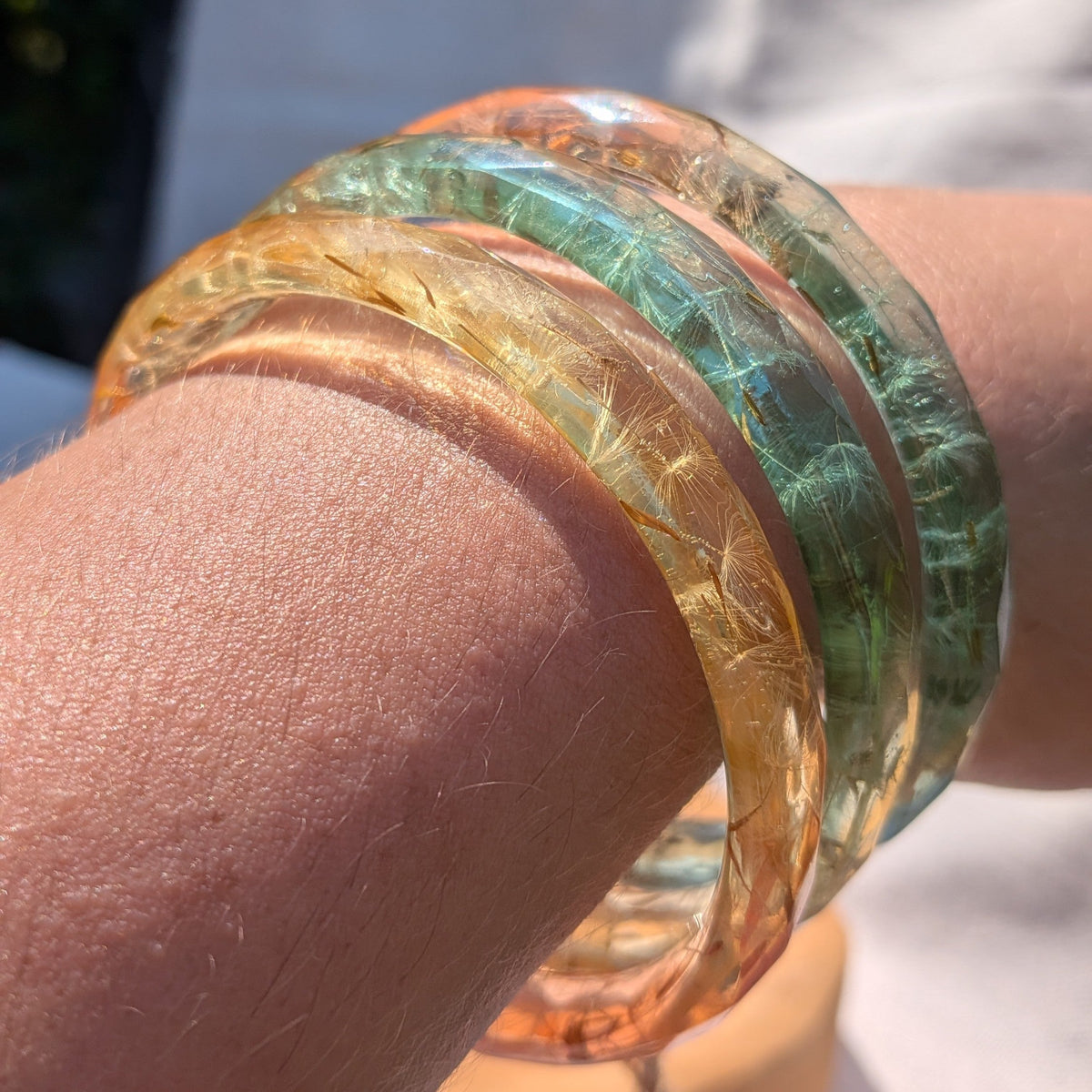 Stacked colourful dandelion seed resin bangles on natural wood by EL-Creations