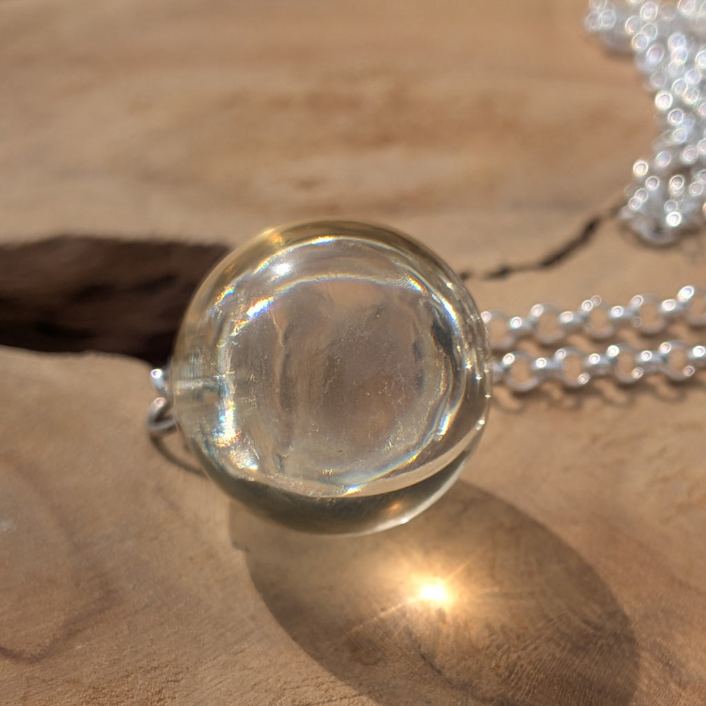 Clear resin ball pendant necklace against bright sky — handmade resin jewelry EL-CreationS Belgium