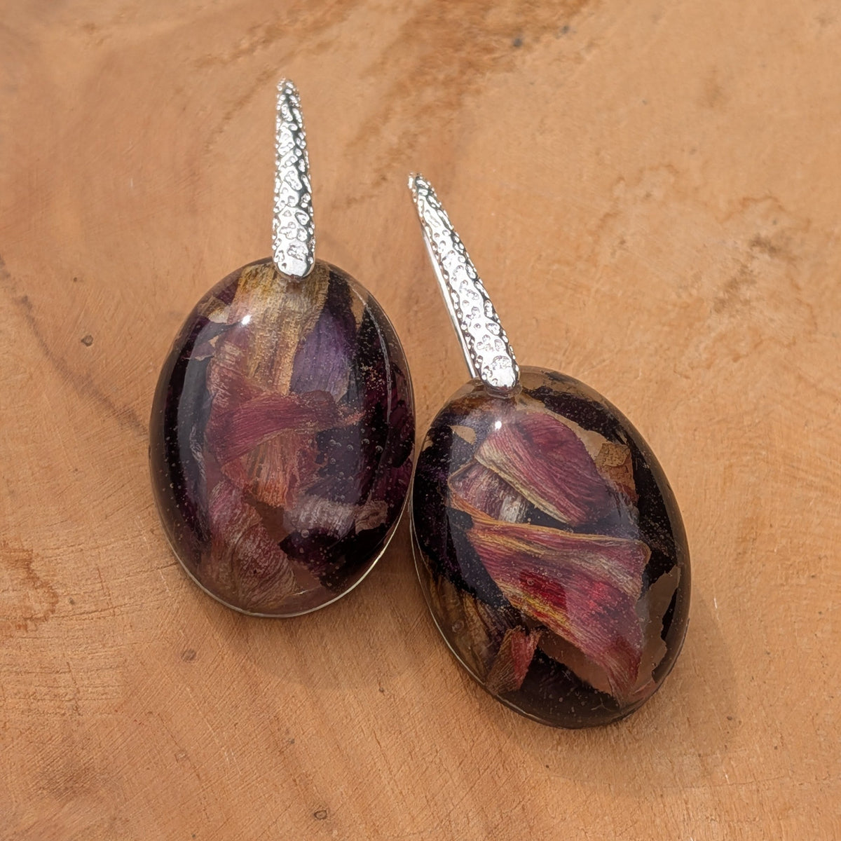 Floral oval resin drop earrings with real tulip petals in burgundy and purple on wooden surface front view – EL-Creations